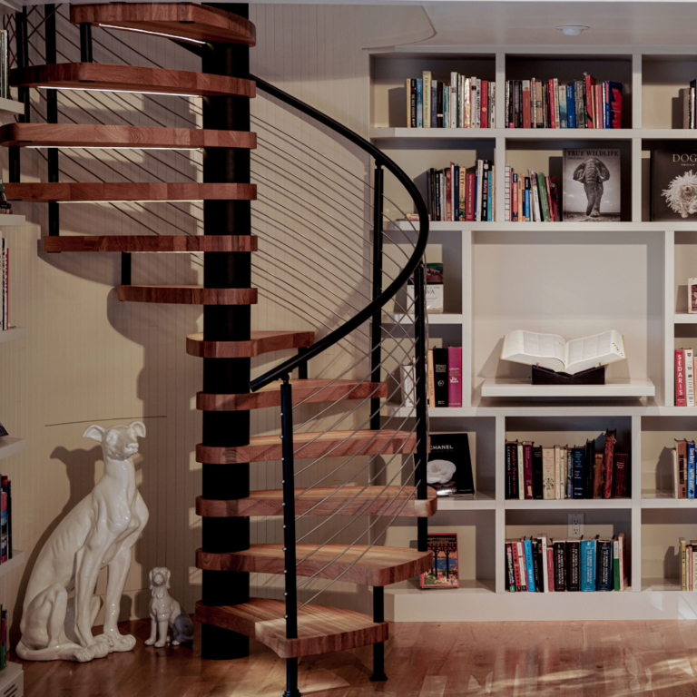 A spiral stair with rod infill turns beside a full white bookcase