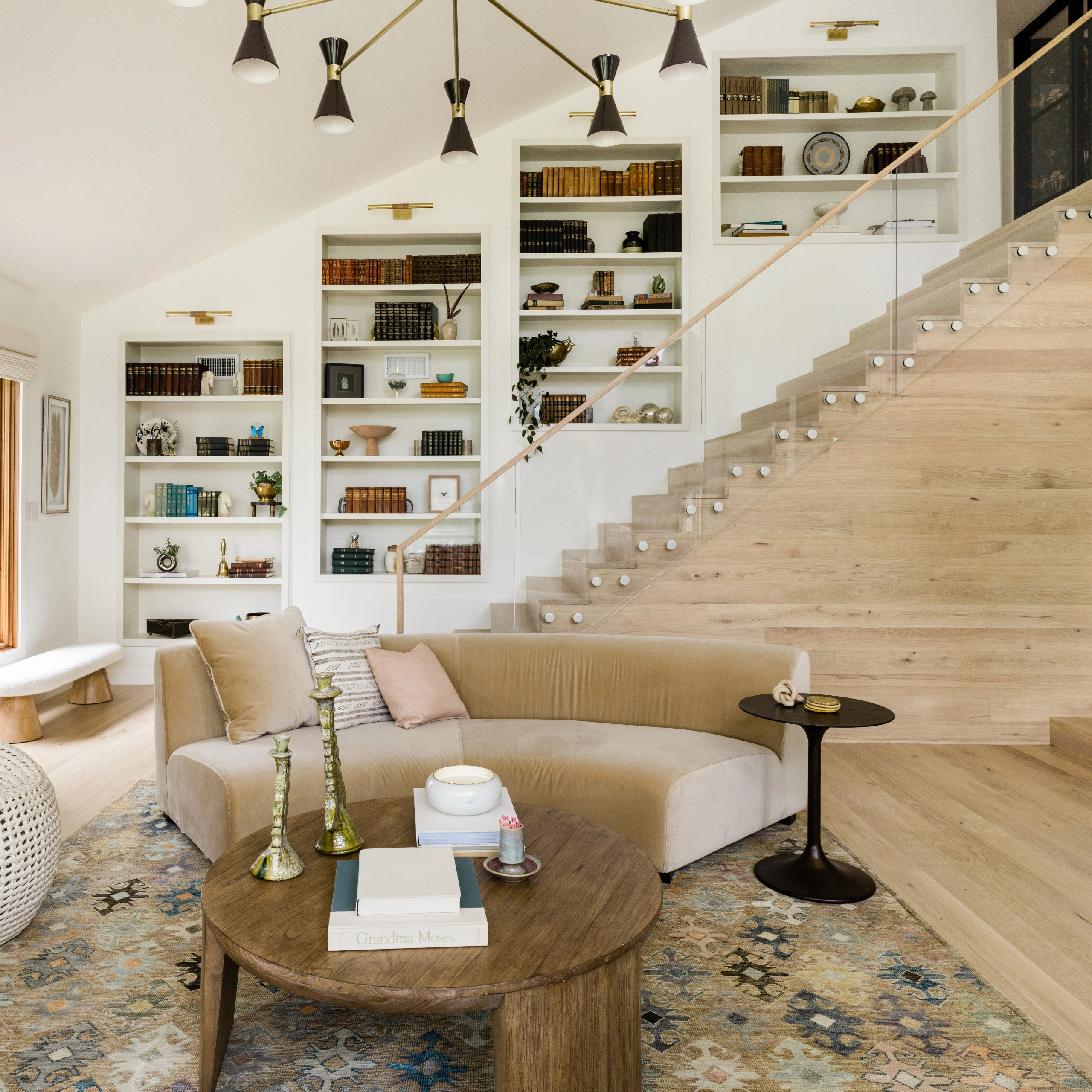 A glass railing climbs past shelves above a curved sofa and low table