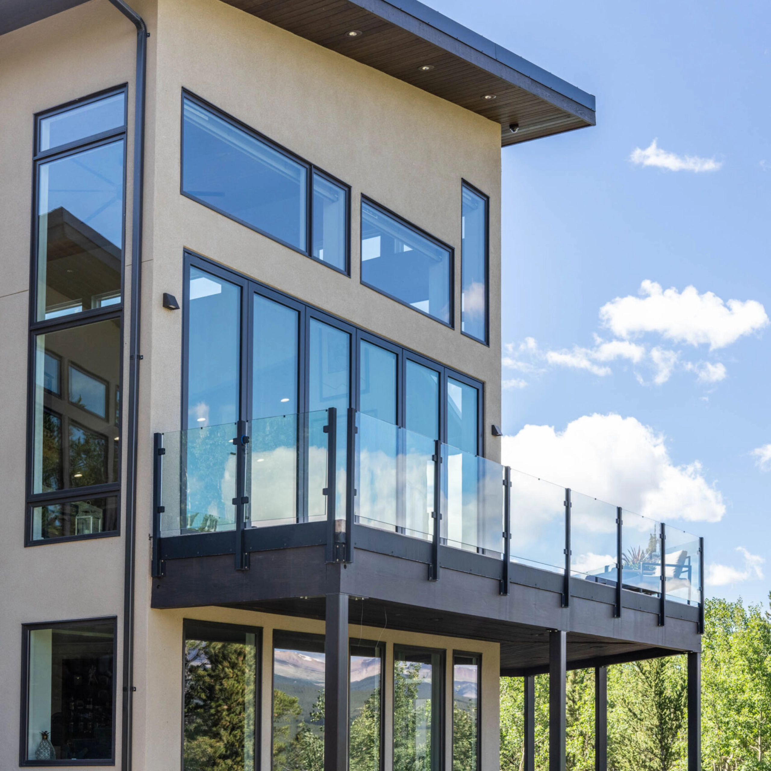 Glass railing on black posts wraps a second-story balcony on a stucco home