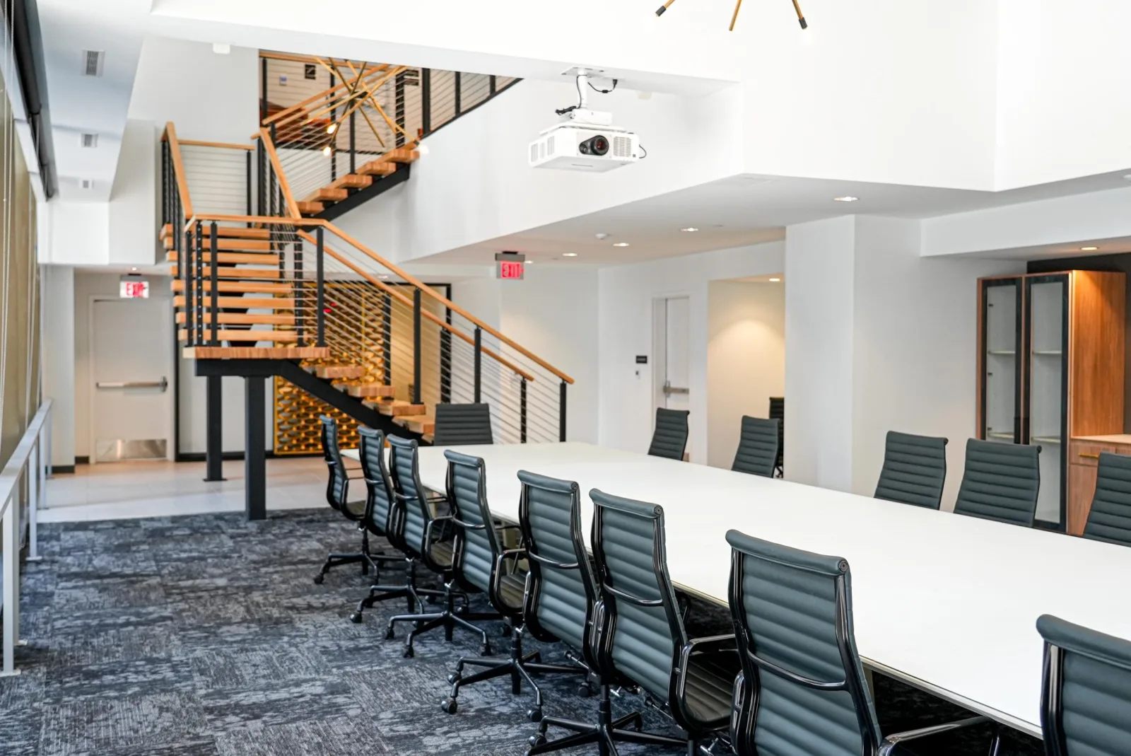 Long conference table and black chairs with the floating stair behind on carpet