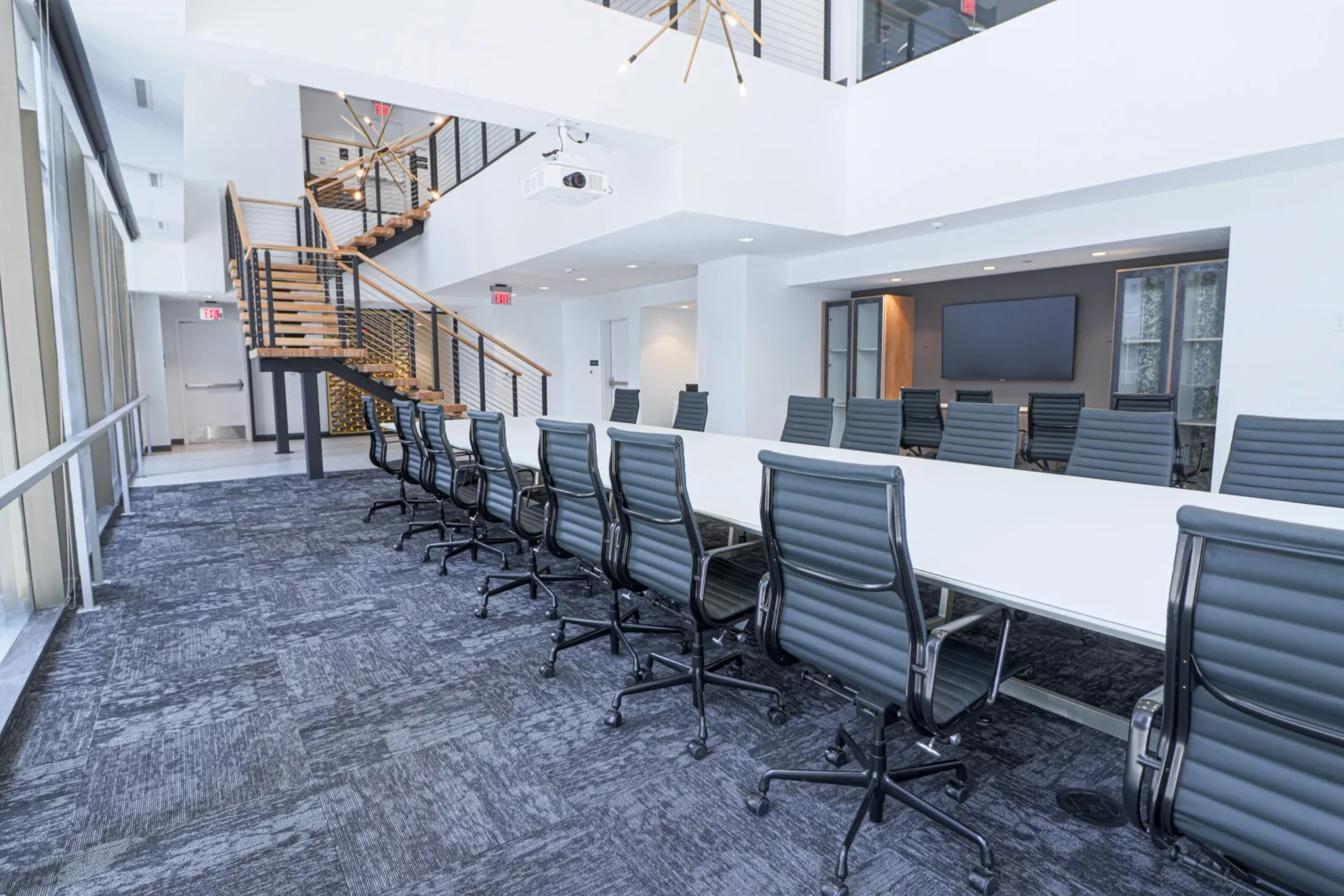 Meeting room with rolling chairs, wall-mounted screen and the stair beyond