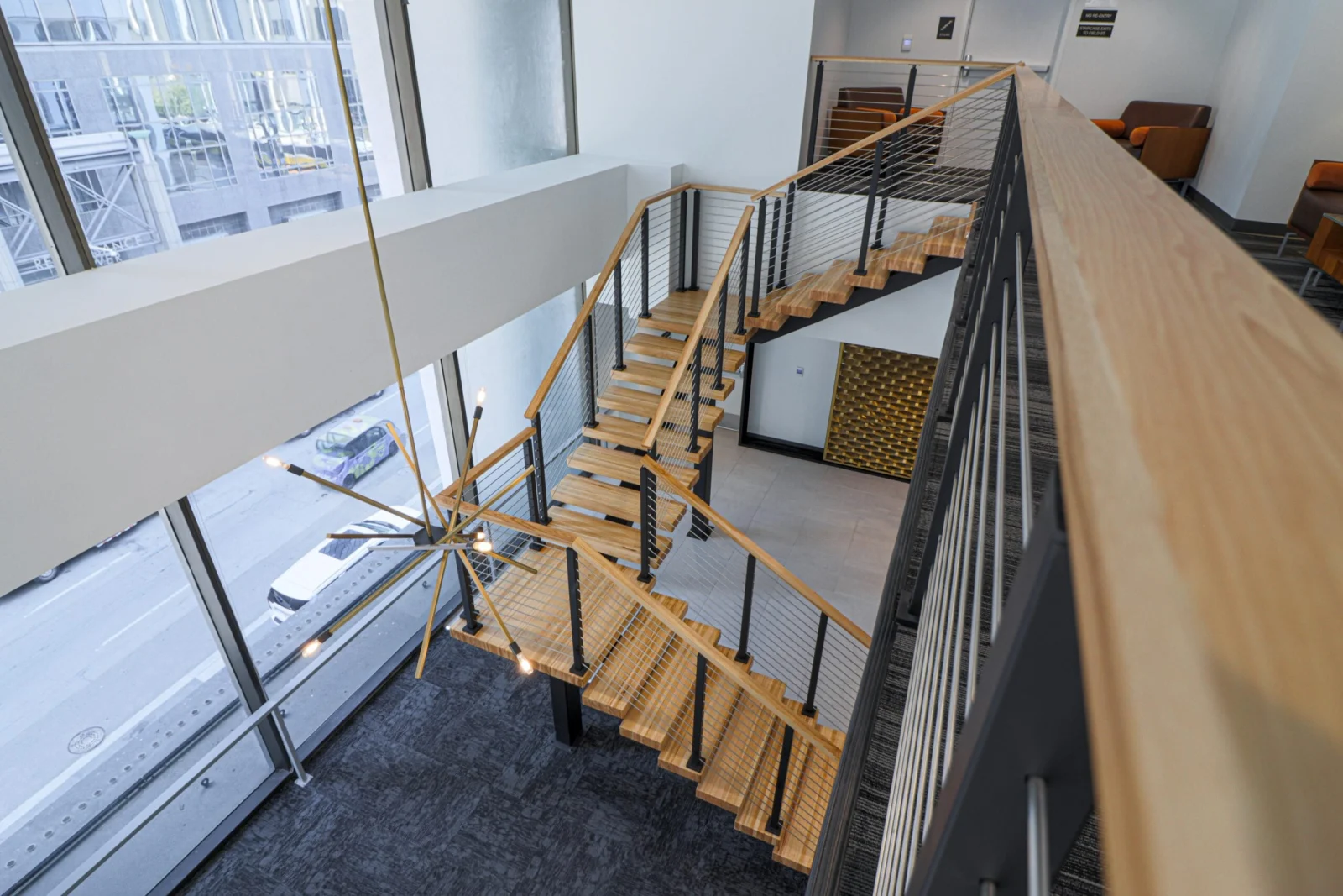 View down the stair toward floor-to-ceiling windows and the street below