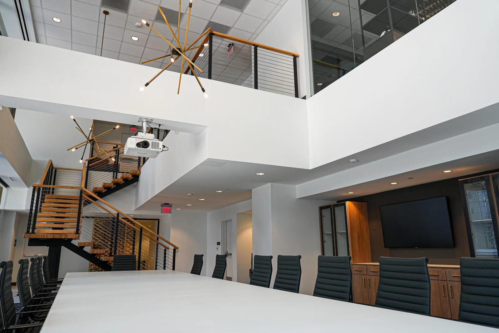 Two-story office atrium with cable railing balcony above a long white meeting table