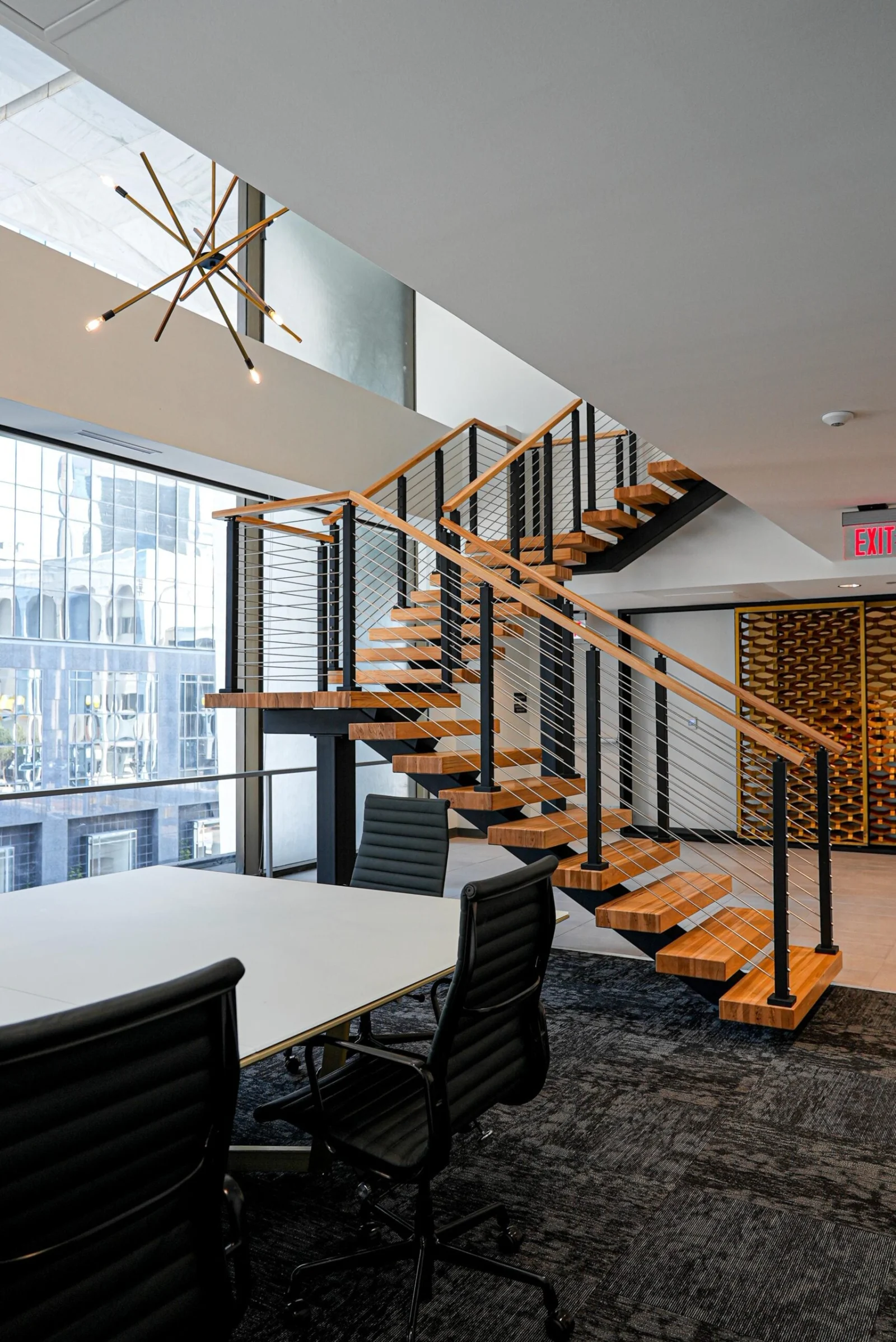 Wood-tread floating stair with black cable railing rising past a conference table