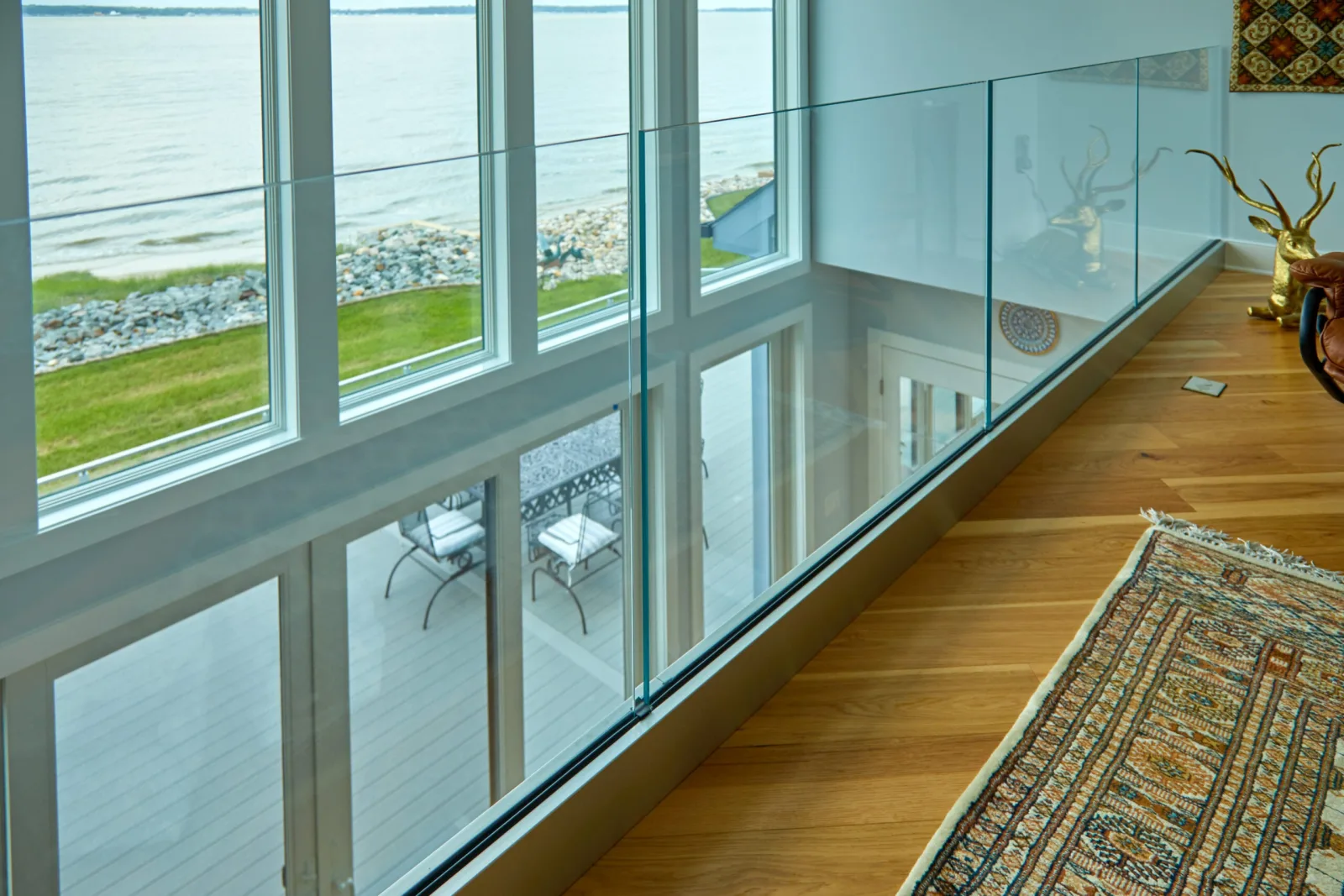 Interior overlook lined with frameless glass panels above a two-story window wall facing water