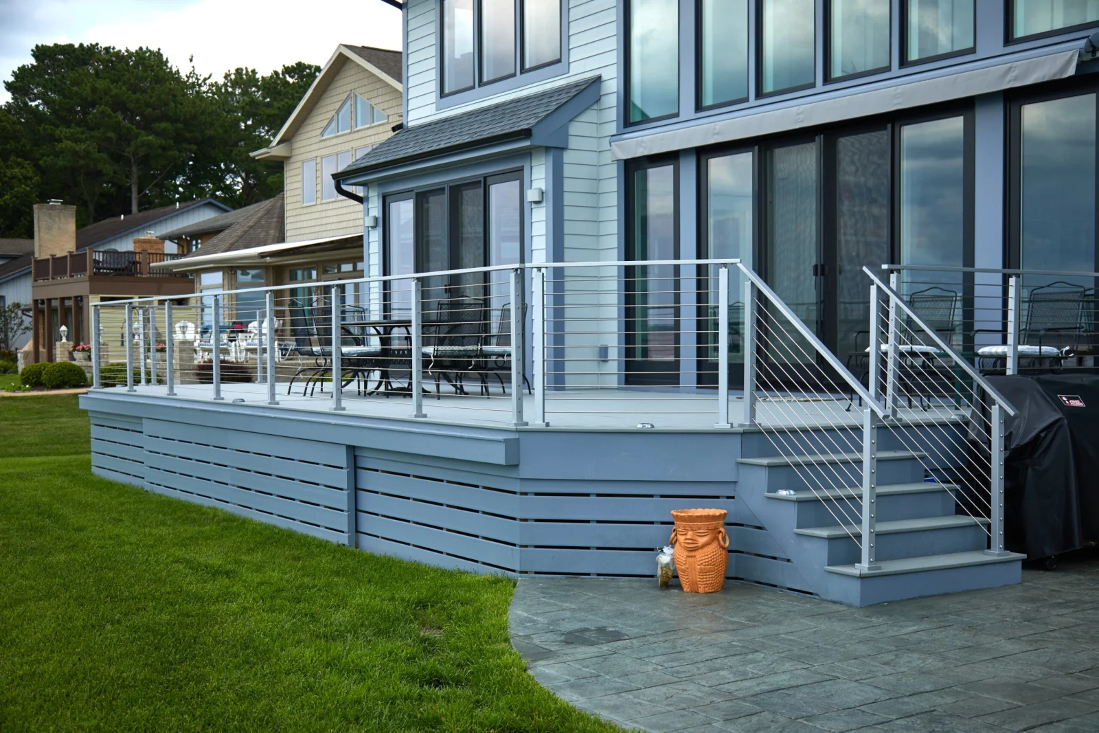 Horizontal rods in metal posts wrap a gray deck with steps to a paver patio