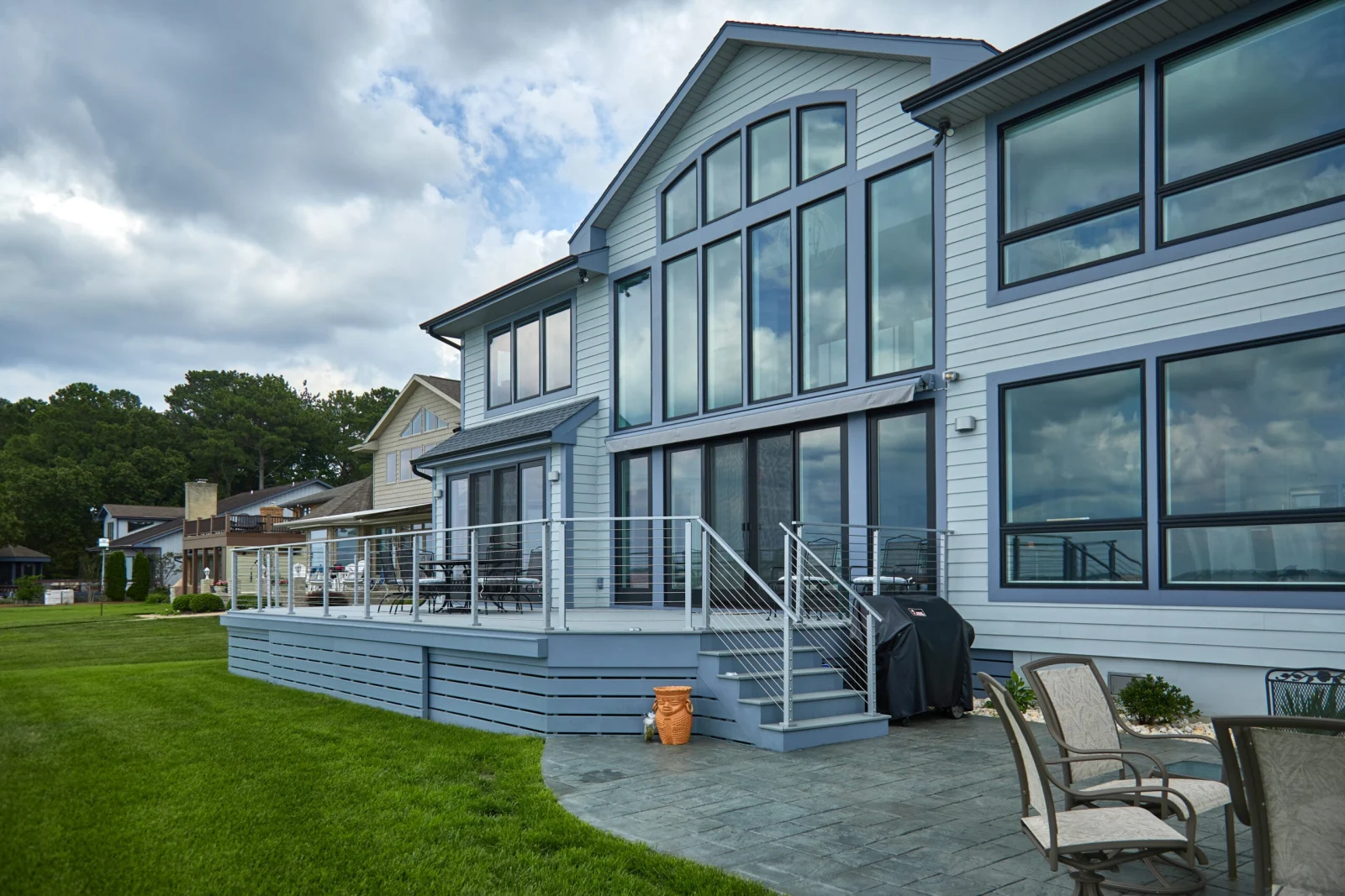 Blue-sided waterfront home with a raised deck and metal railing running along the lawn
