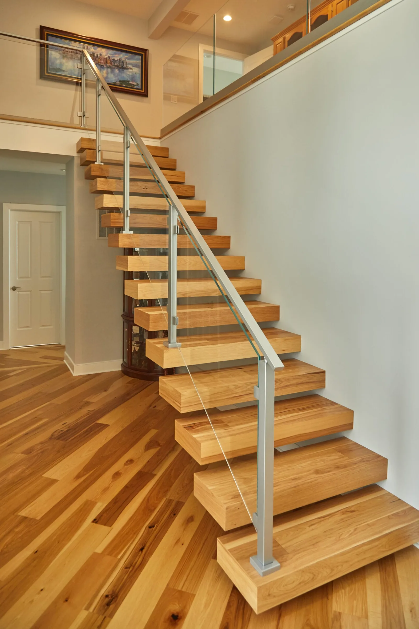 Wood-tread floating stair with horizontal rod infill and slim metal posts in an entry