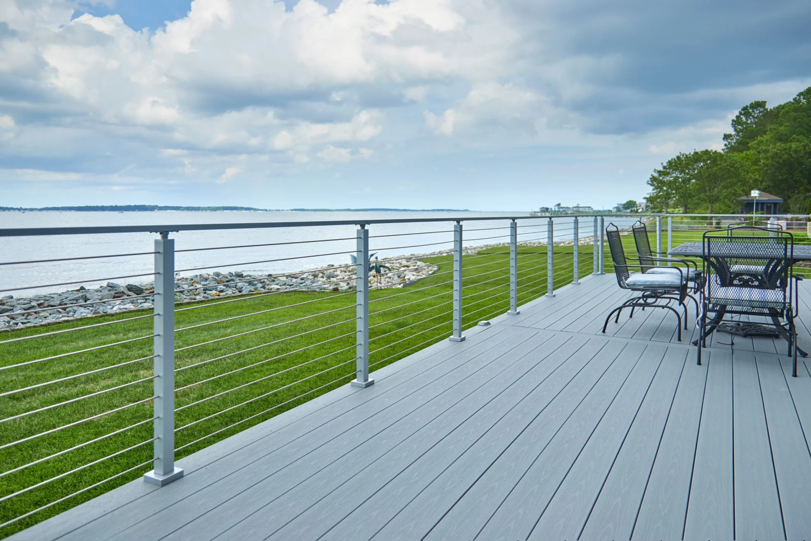 Gray deck edged with horizontal rod railing on slim posts above a rocky shoreline