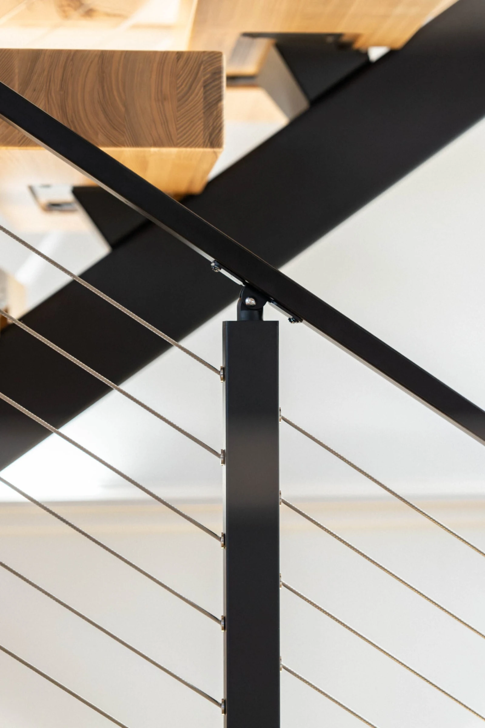 Upward angle along a black handrail crossing a post, wood stair treads overhead