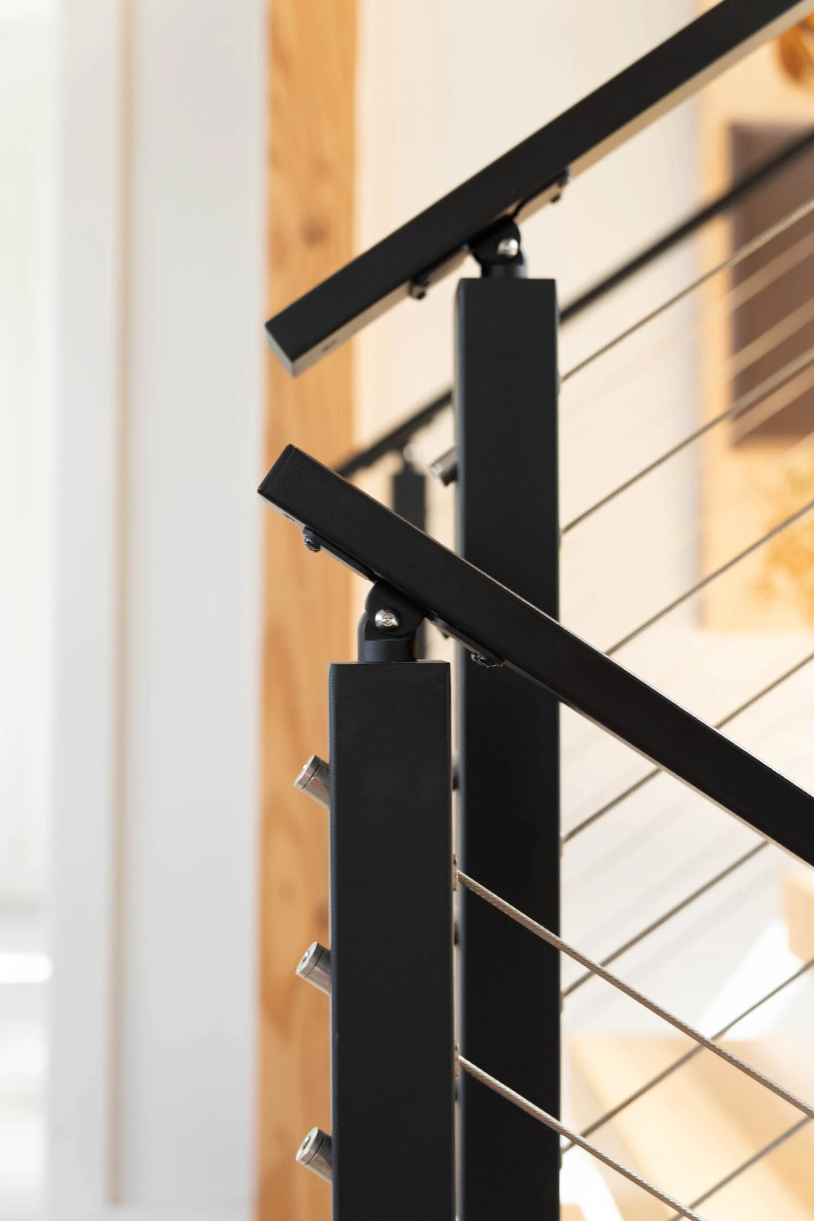 Close view of black posts and flat top rails meeting above taut stainless cables