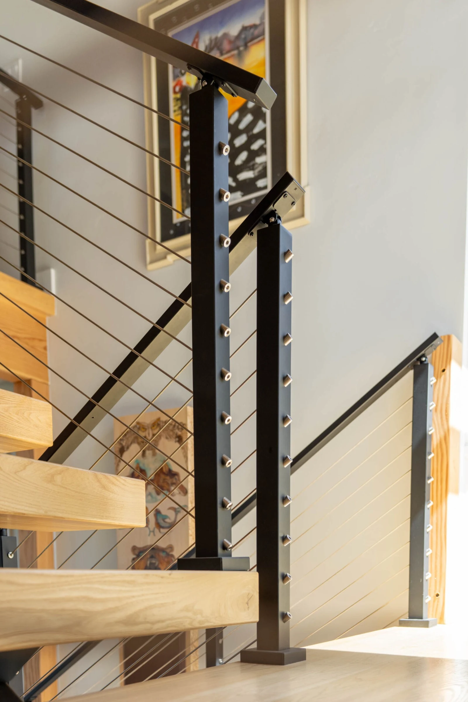 Black newel posts anchor angled cable runs beside pale wood treads at a landing