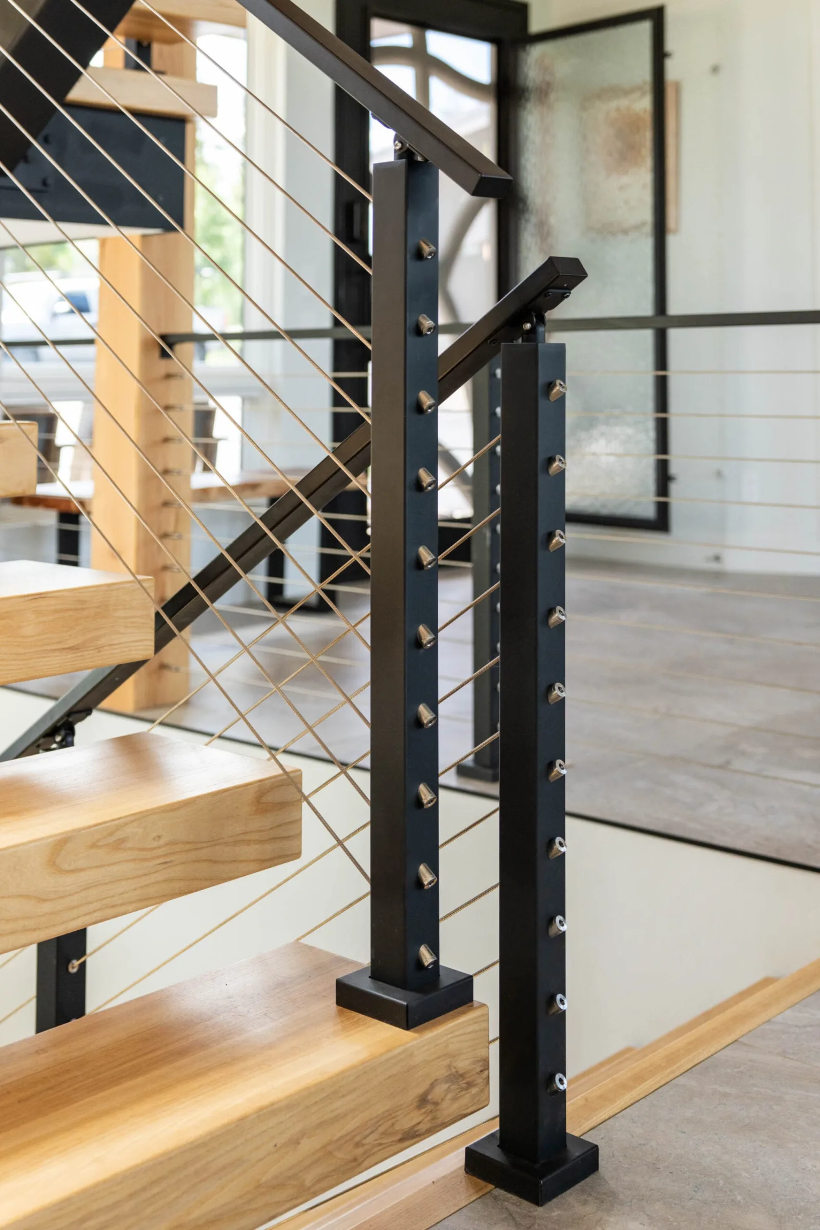 Post bases mounted on wood treads, cable lines fanning toward the floor below