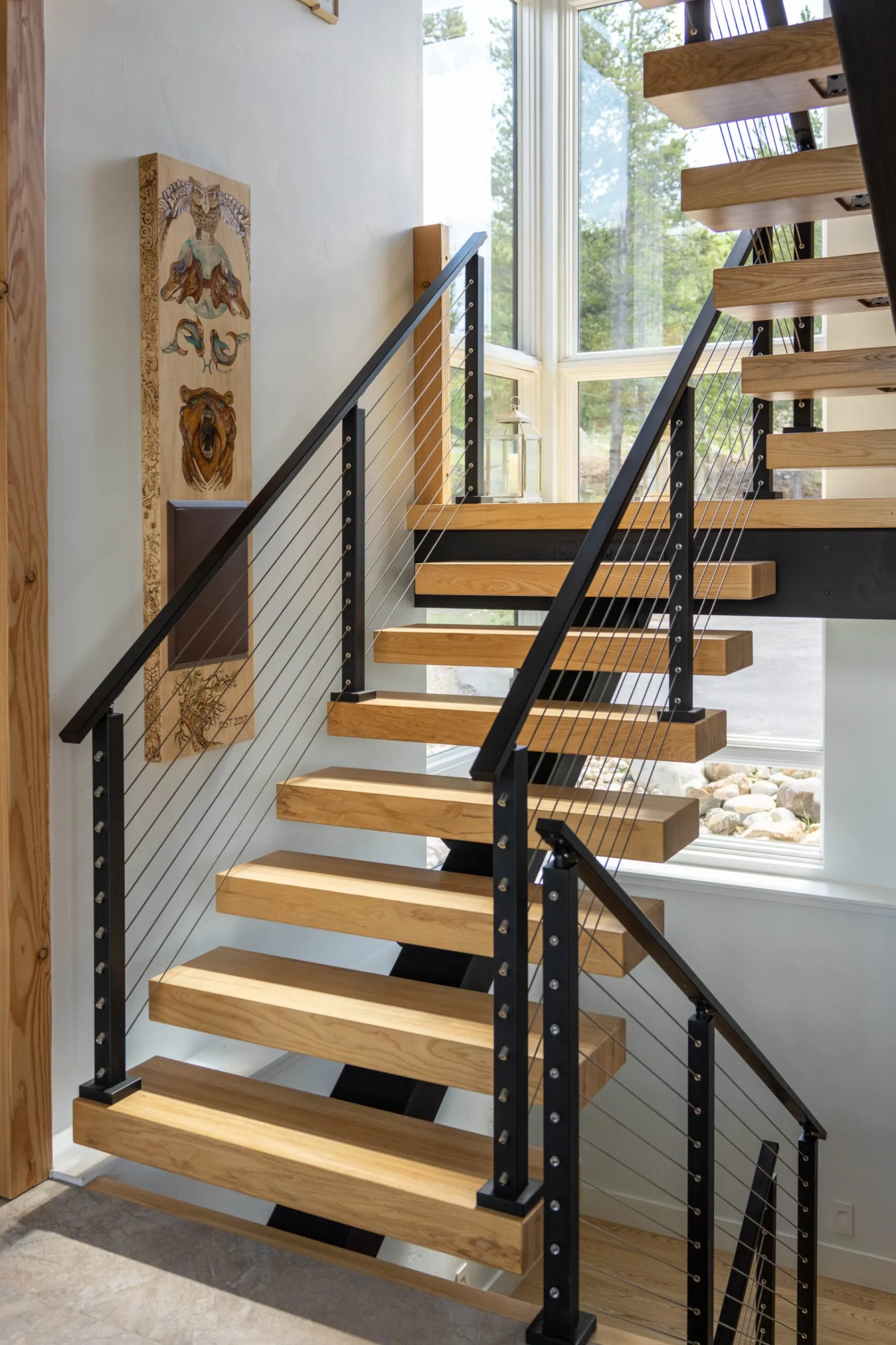 Cable infill in black posts follows two flights of a wood-tread stair