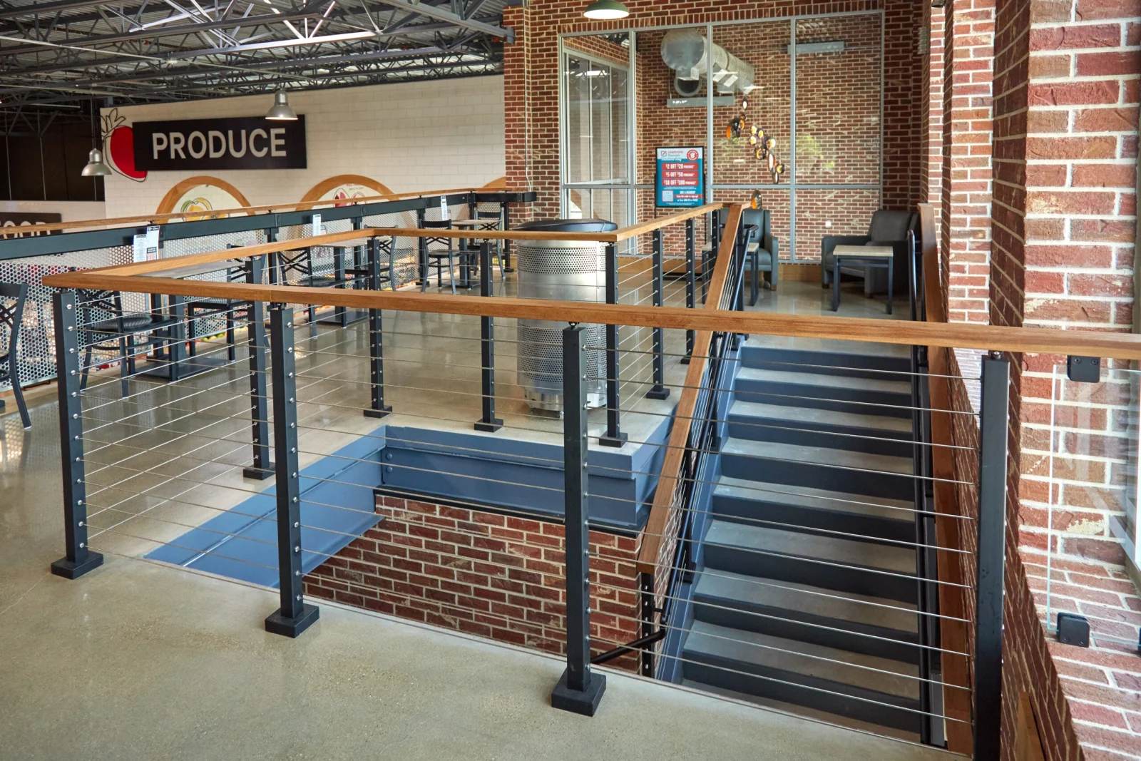 Cable railing with a wood top rail edging a mezzanine above the produce aisle