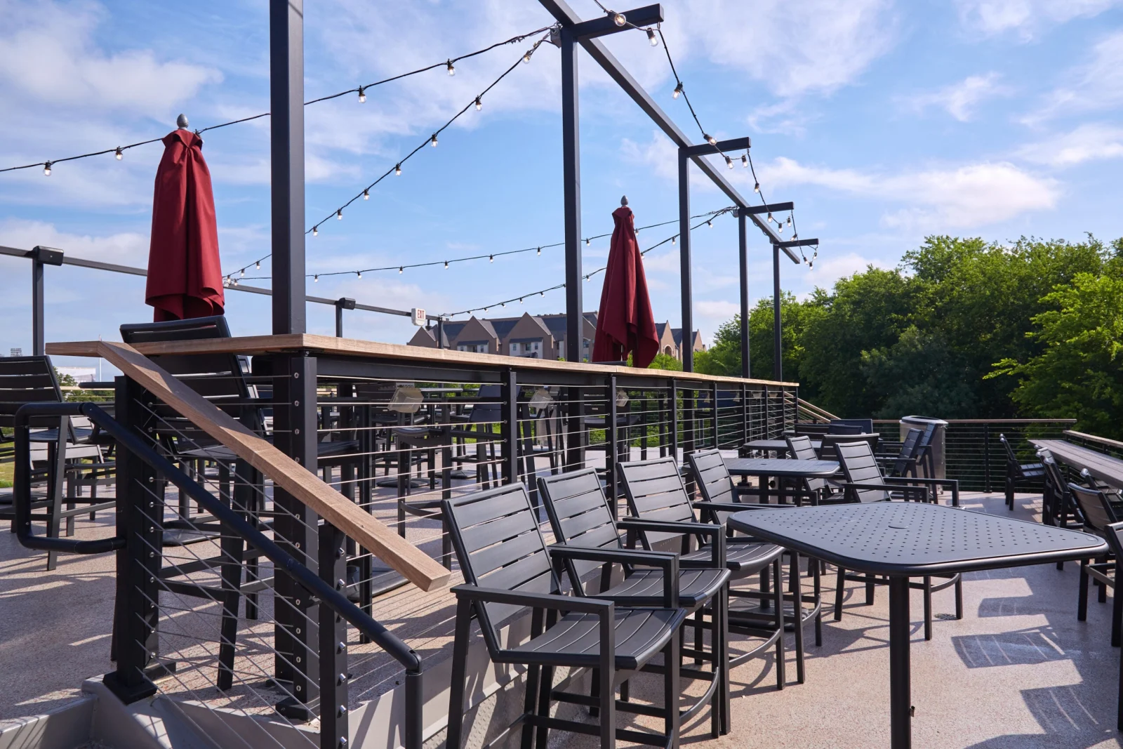 Wood-capped cable railing along a patio terrace with umbrella tables and open sky