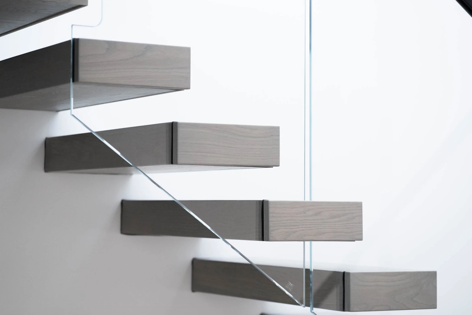 Cantilevered treads floating from a white wall behind a frameless glass panel