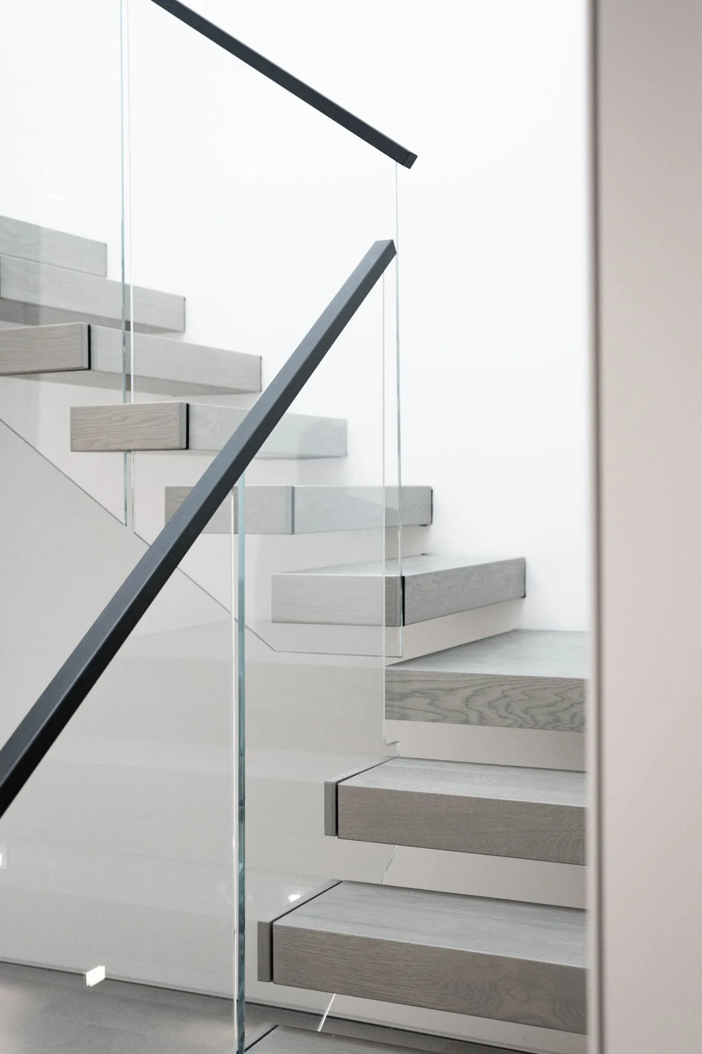 Stair run climbing past a glass balustrade with a black angled handrail