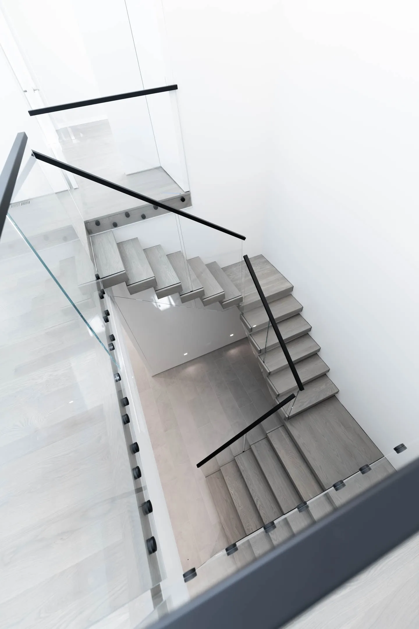 Looking down a stairwell at cantilevered gray treads behind glass railing panels