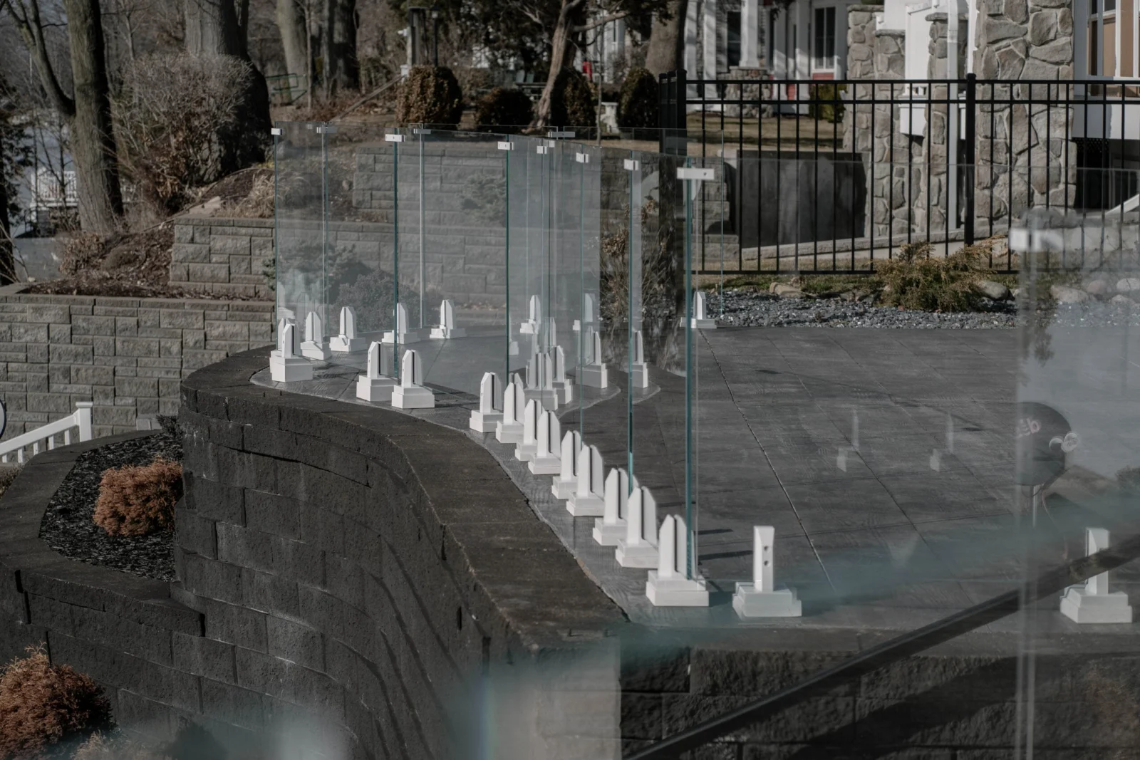 Glass railing curving along a stone retaining wall in a bare winter yard