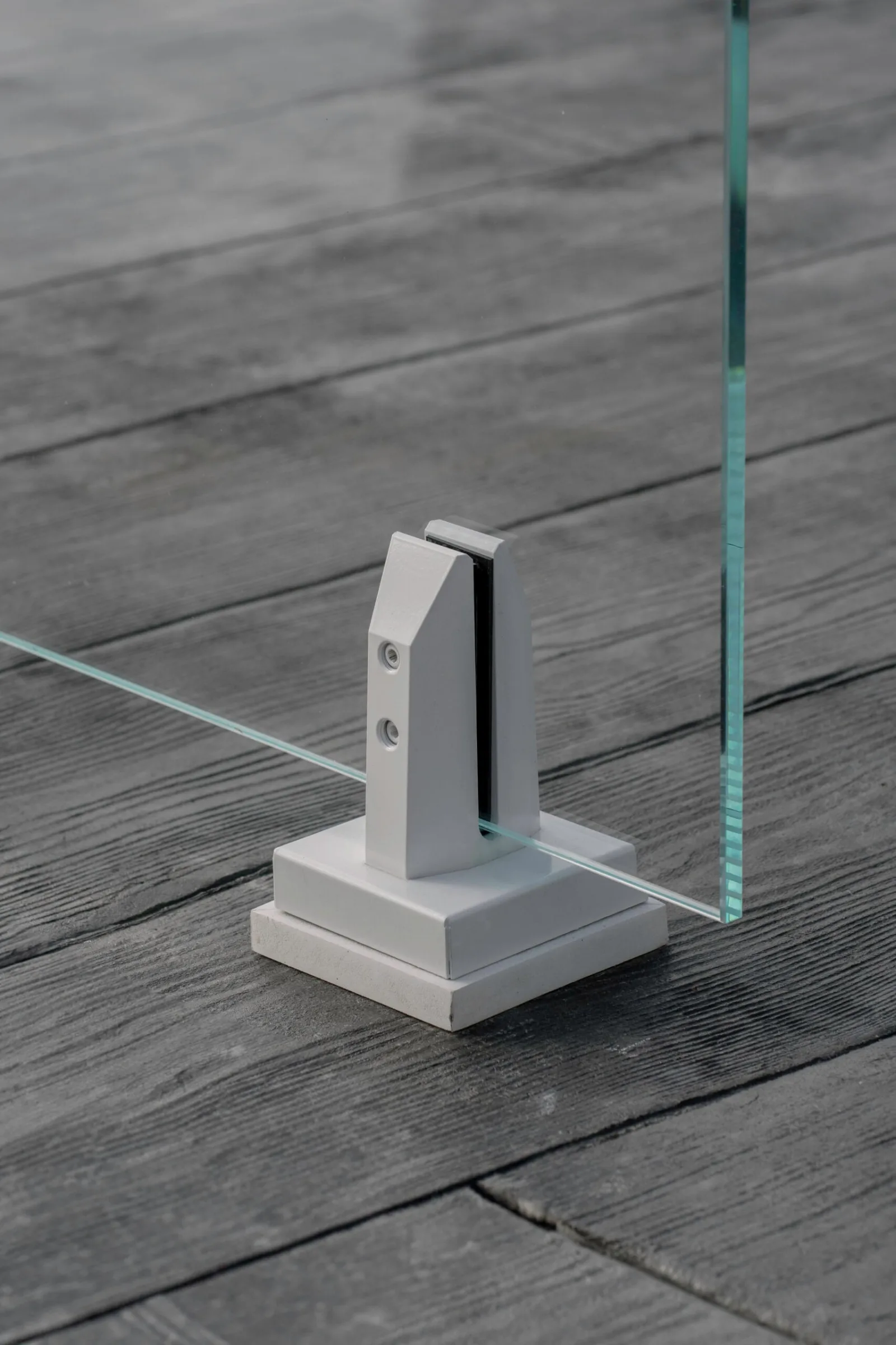 White base clamp set on dark gray decking supporting a glass panel