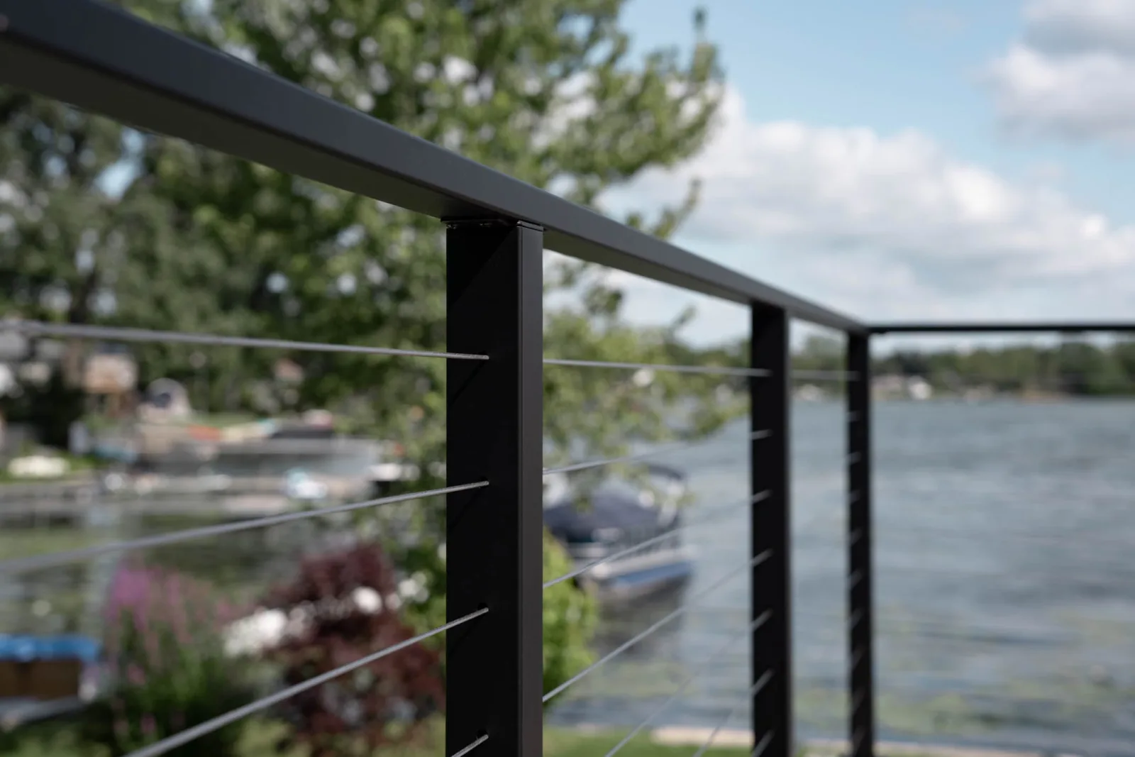 Close view down a black top rail and cables toward a moored boat on the lake