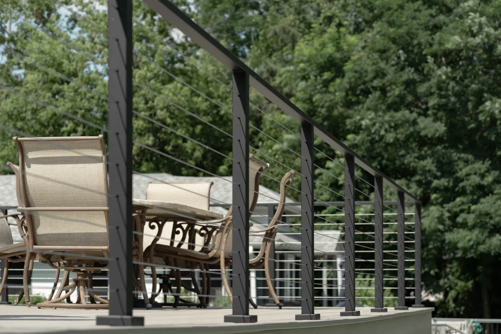 Low angle down the railing line past patio chairs and green trees