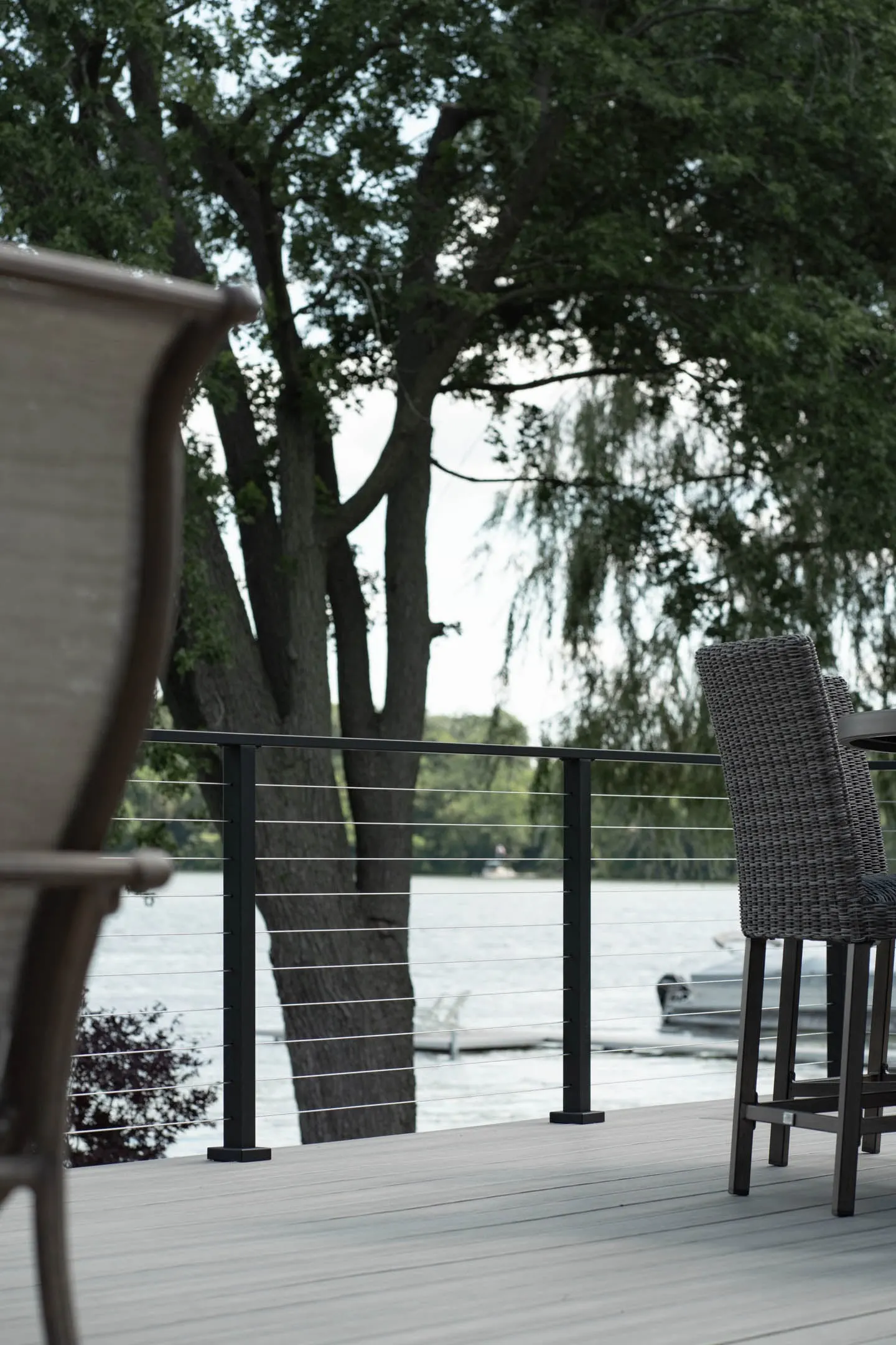 Railing framing willow trees and a lakeside dock beyond bar-height seating