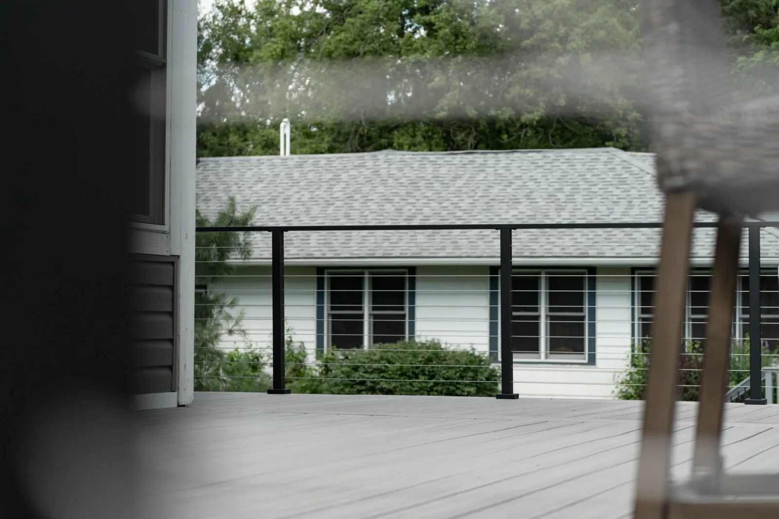 Railing crossing the deck with a neighboring roofline beyond the cables