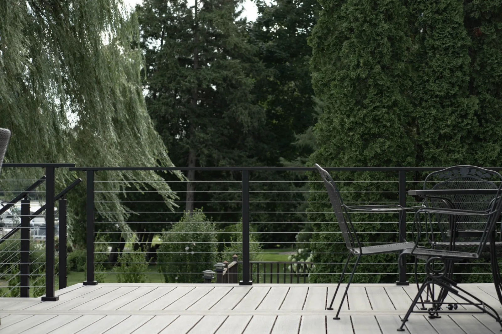Cable railing backed by willow and evergreen trees at the yard edge