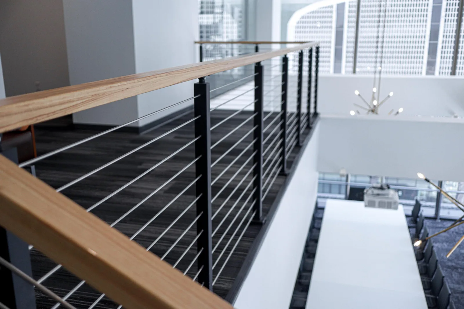 Wood-capped cable railing along an office mezzanine with city towers beyond curved glass