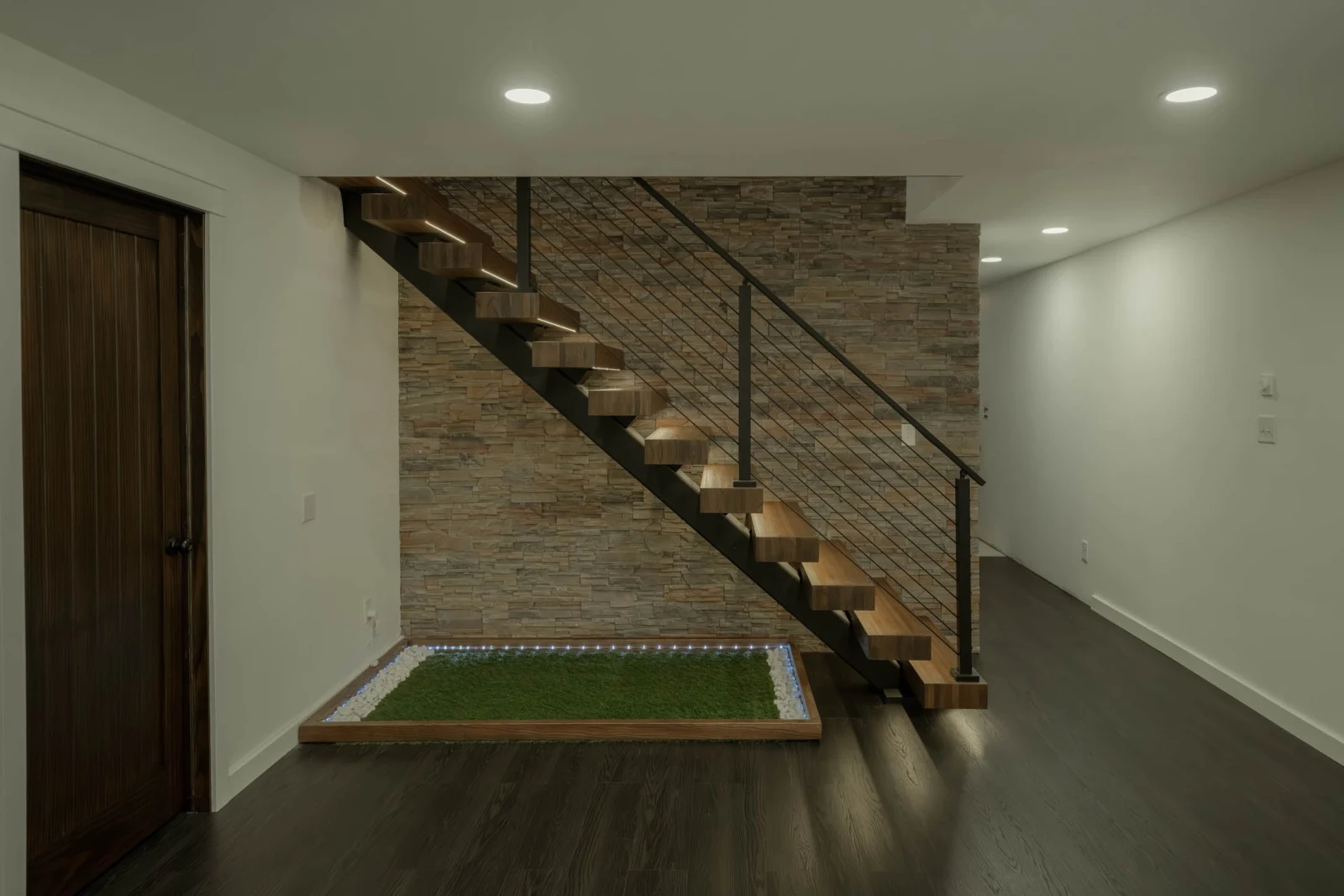 Lower-level room with the stair floating above a turf and pebble bed