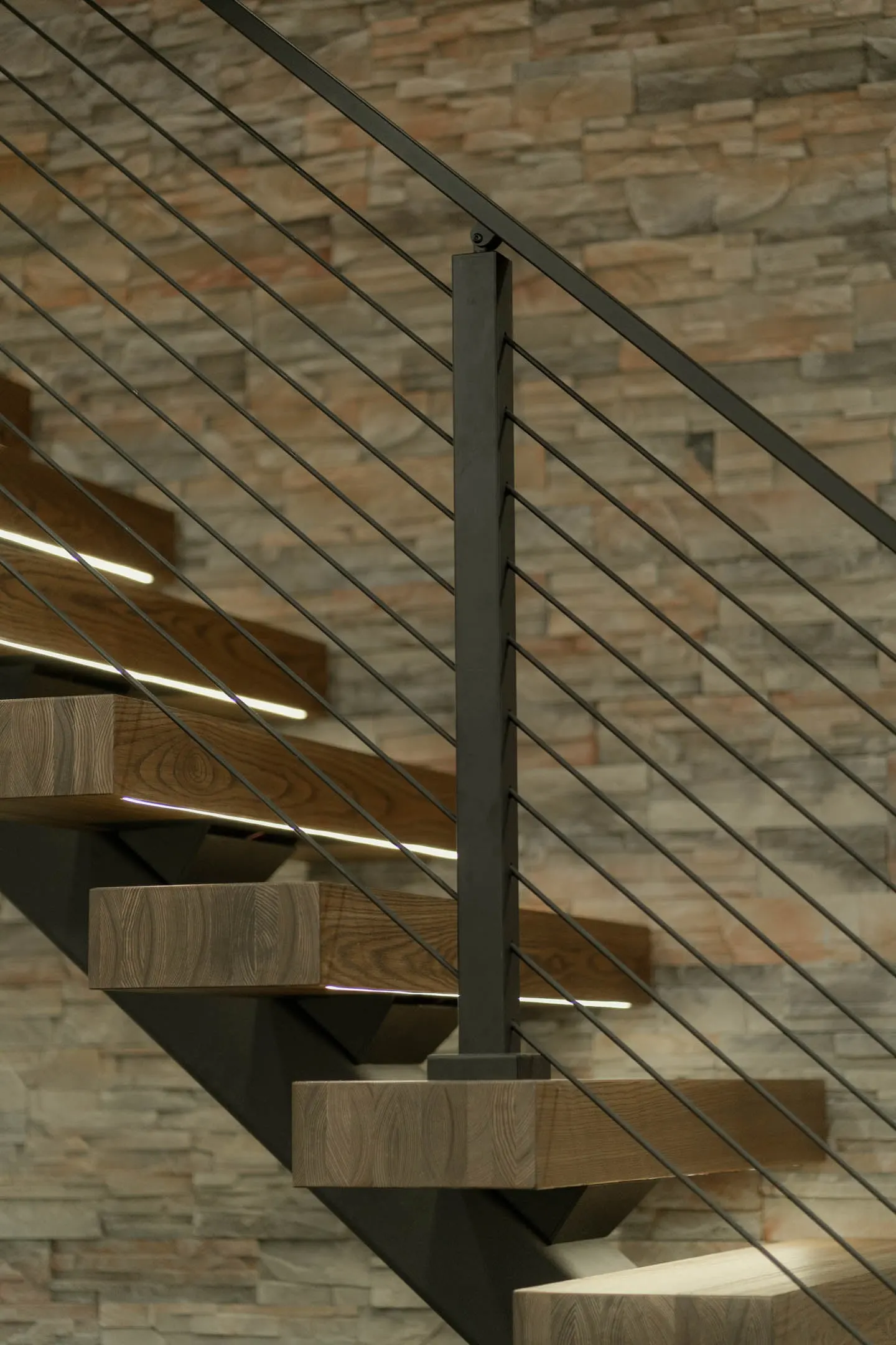 Side profile of cantilevered treads and slender rods set against a stone accent wall
