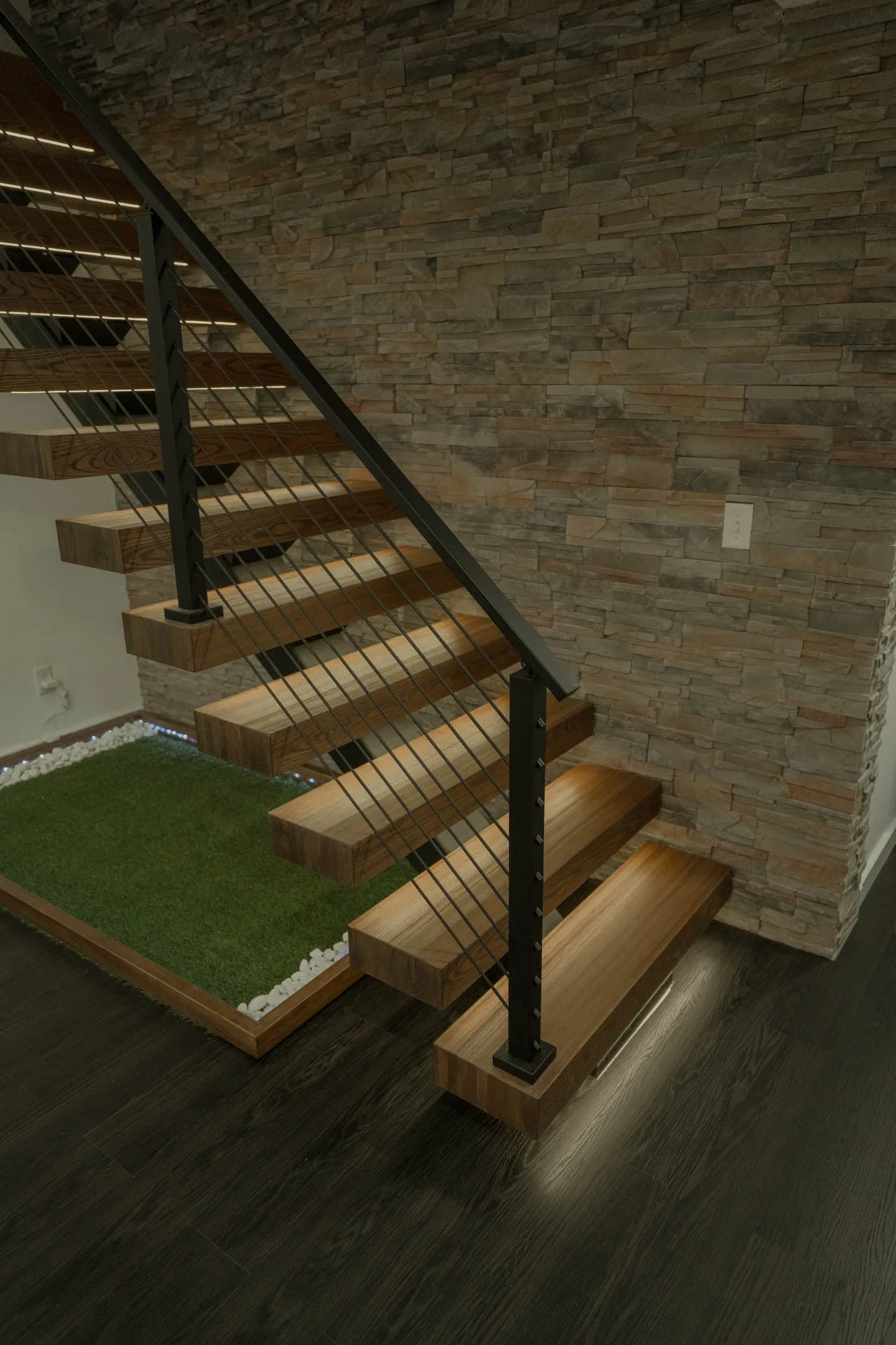Floating stair with wood treads and black rod railing against a stacked stone wall