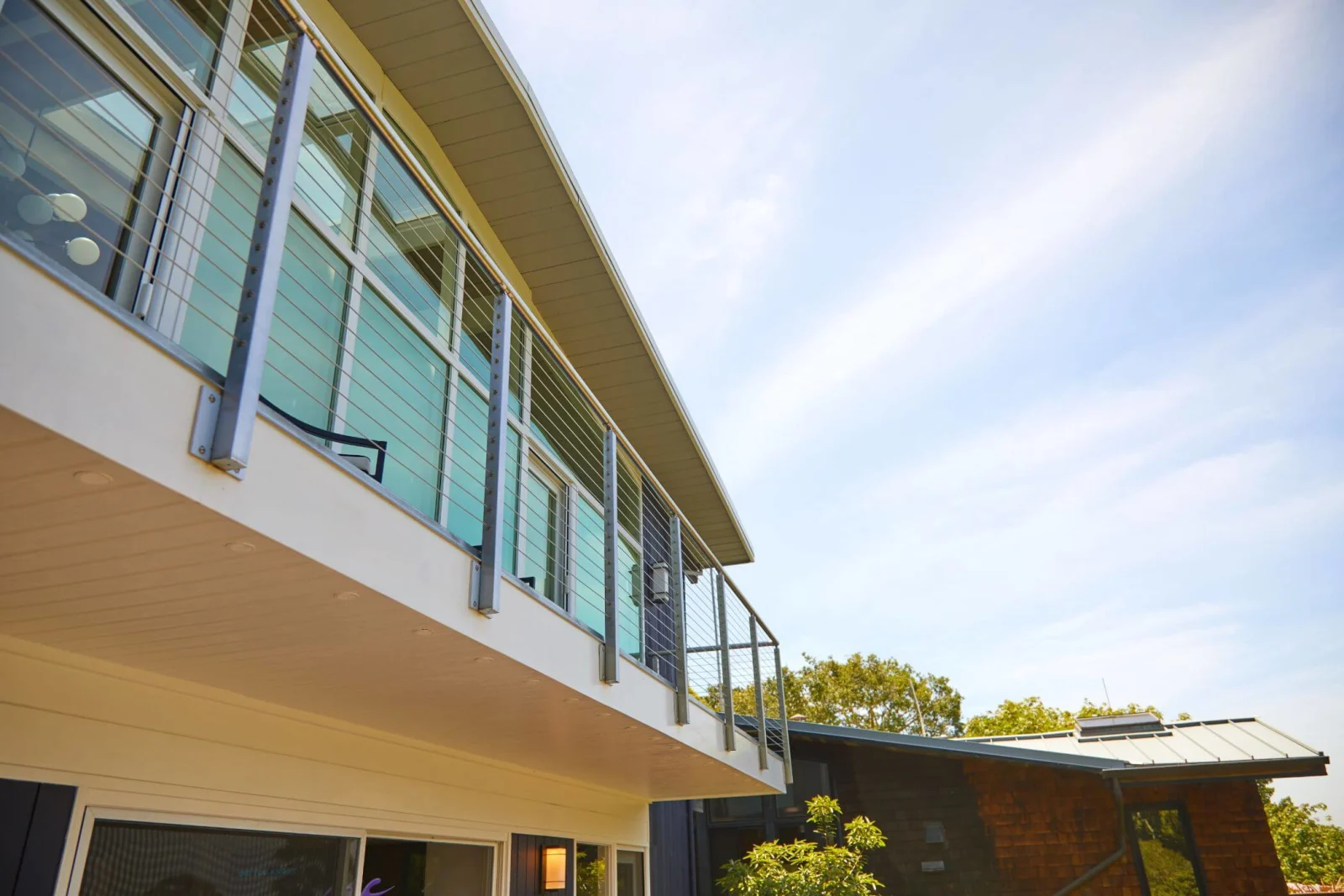 Looking up at side-mounted cable posts wrapping a second-story balcony under clear sky