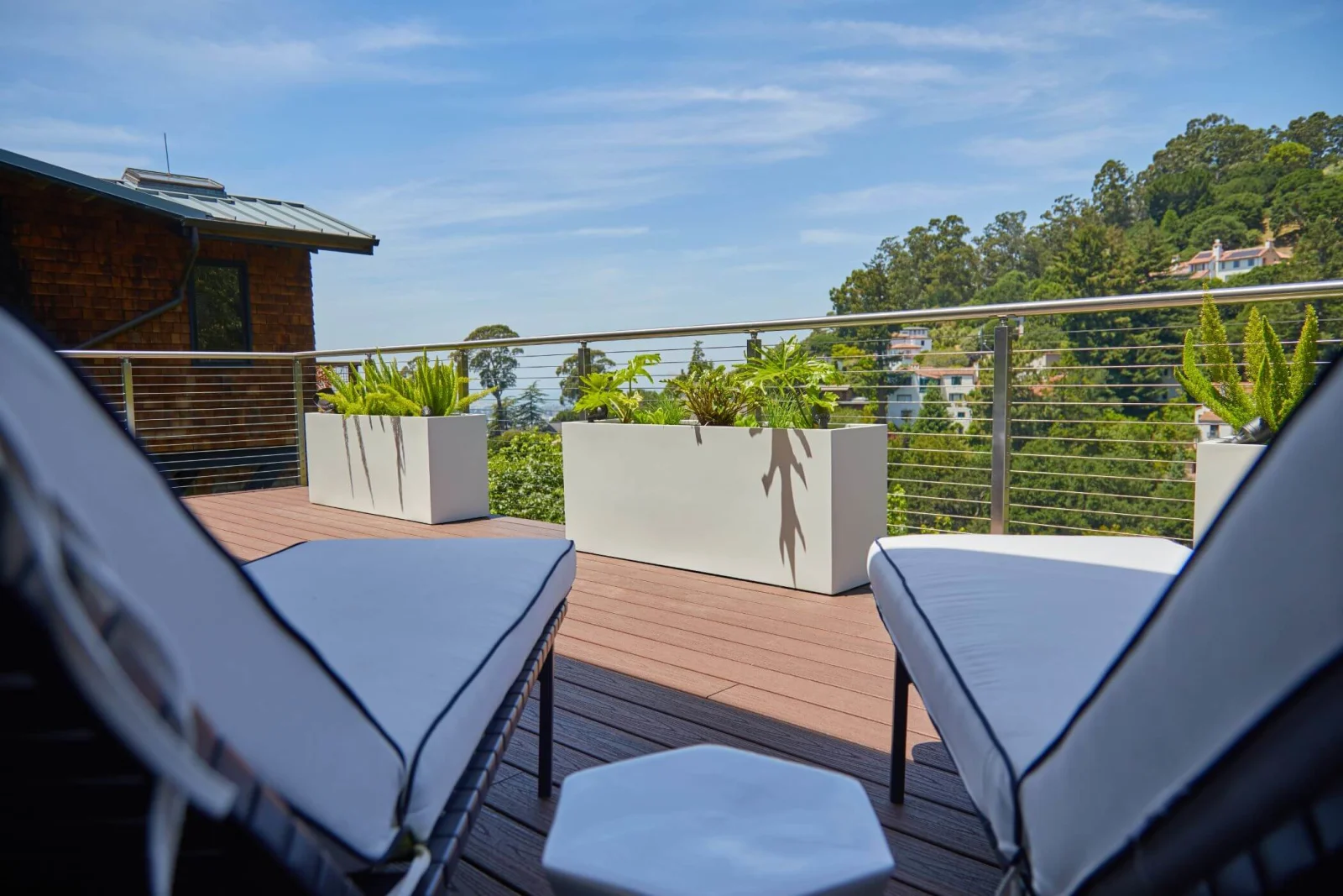Deck loungers and white planters behind cable railing overlooking a wooded hillside
