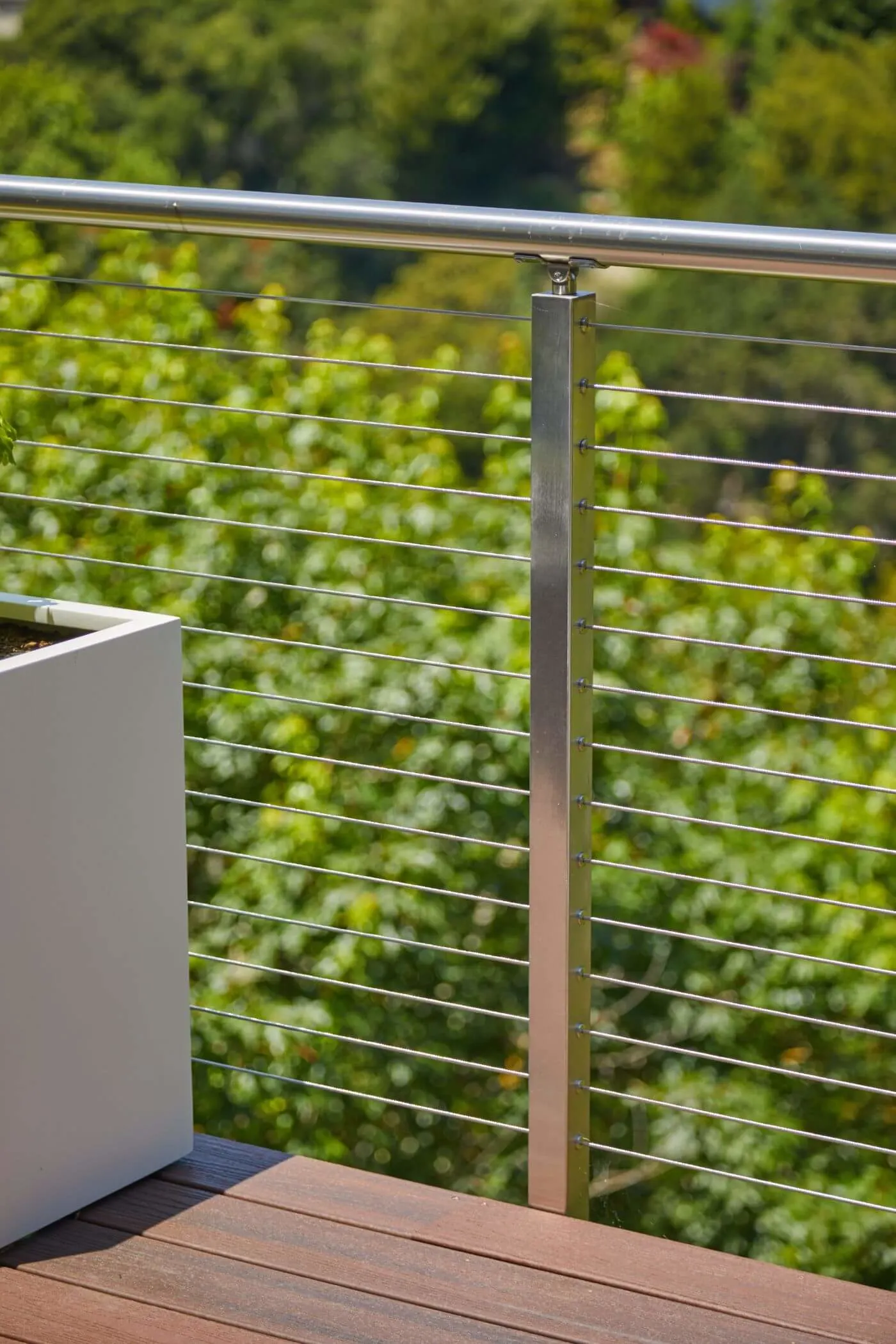 Single stainless post on decking beside a white planter with green hillside behind