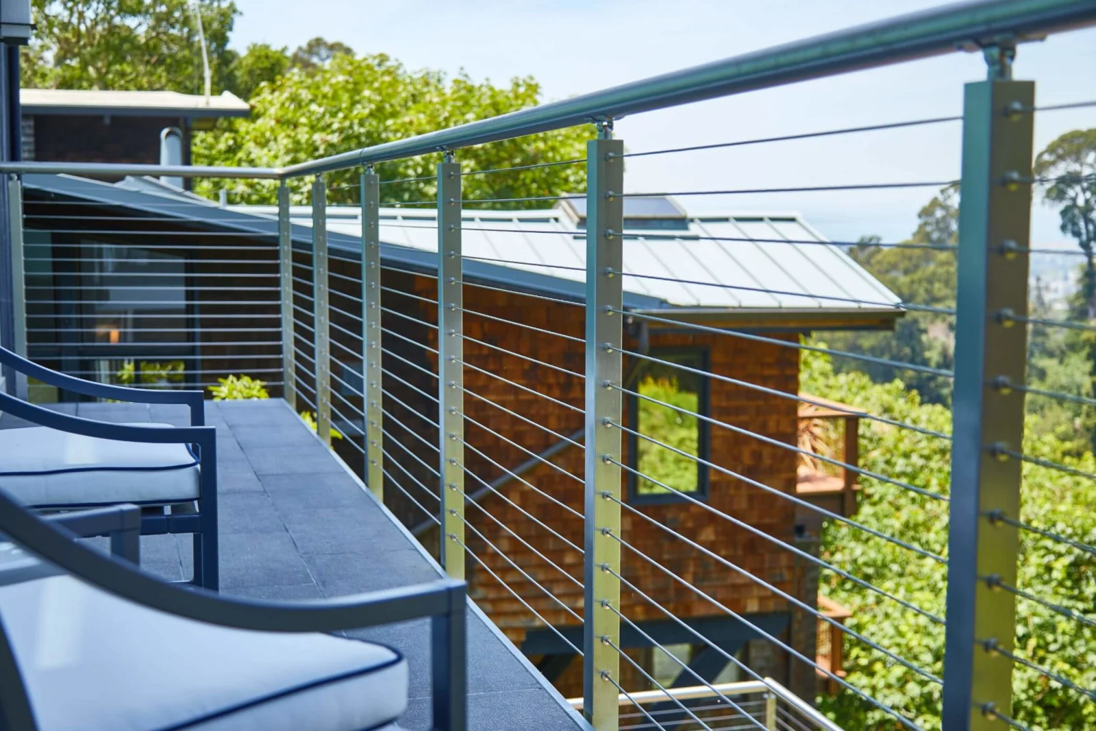 Stainless posts and rounded top rail lining a deck beside a neighboring house