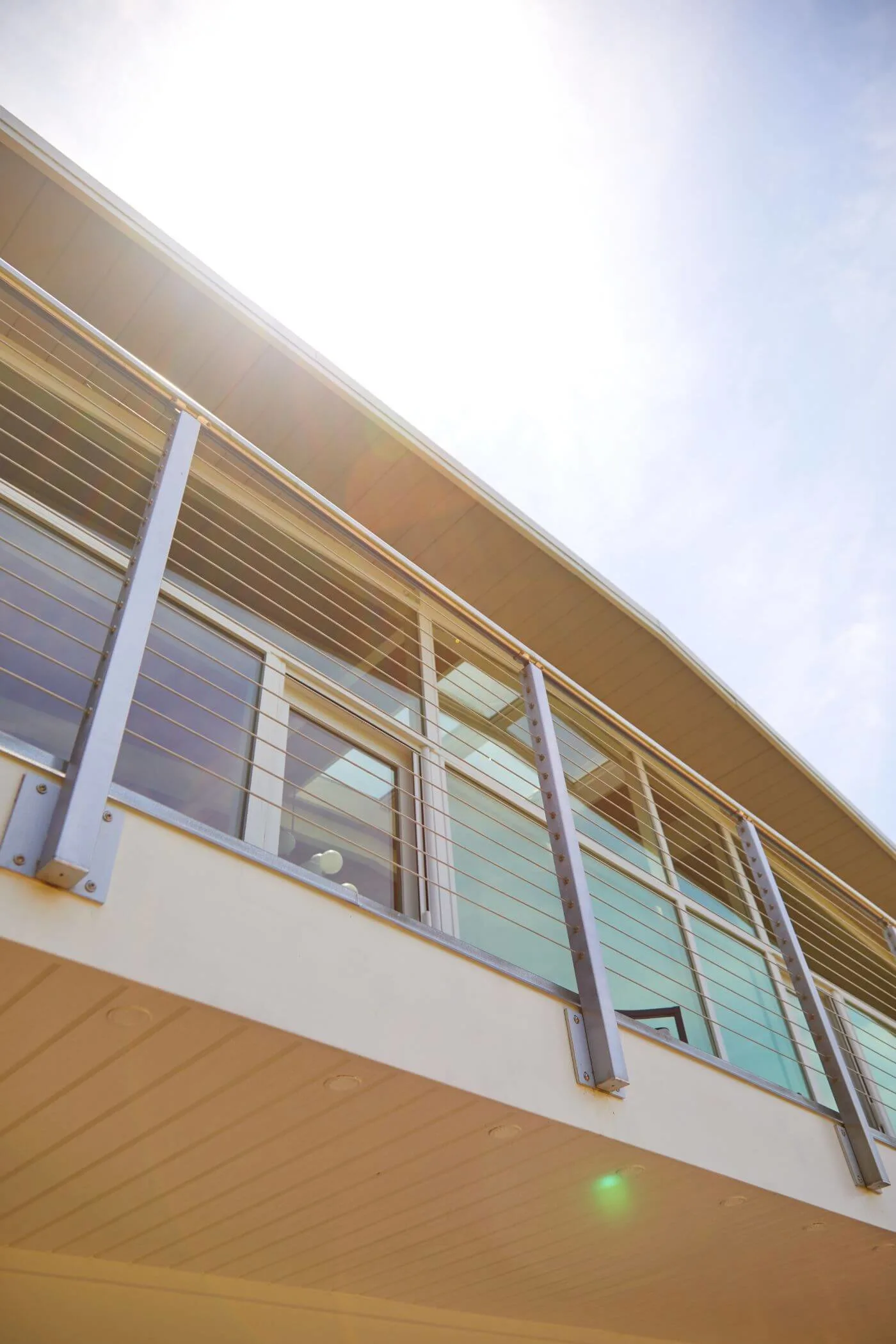 Cable railing seen from below against bright sky along a second-floor walkway