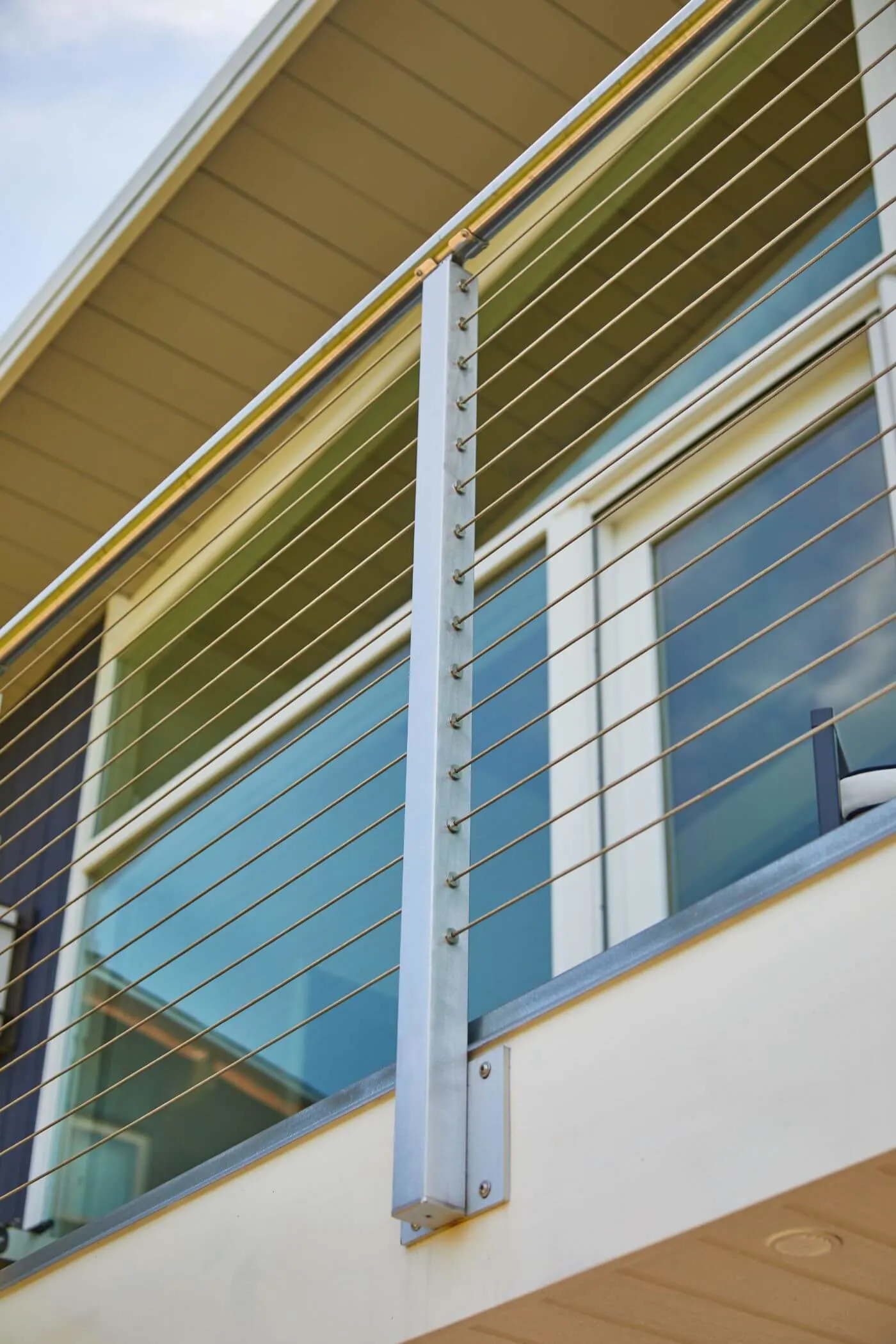Side-mount post bolted to the balcony fascia with cables running past siding
