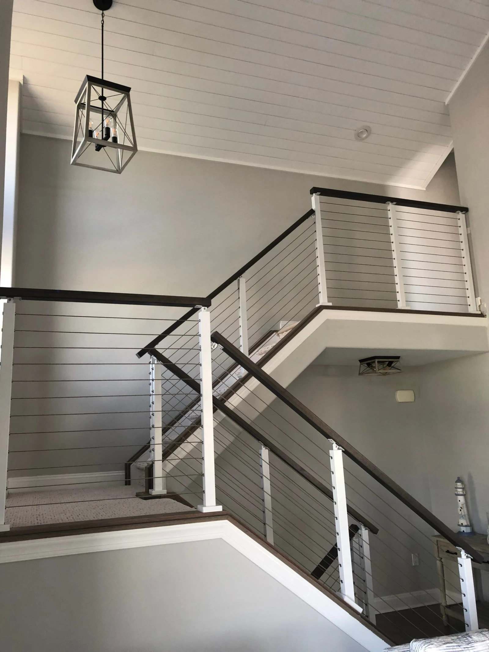 White posts and dark top rails with cable infill turning through a shiplap stairwell