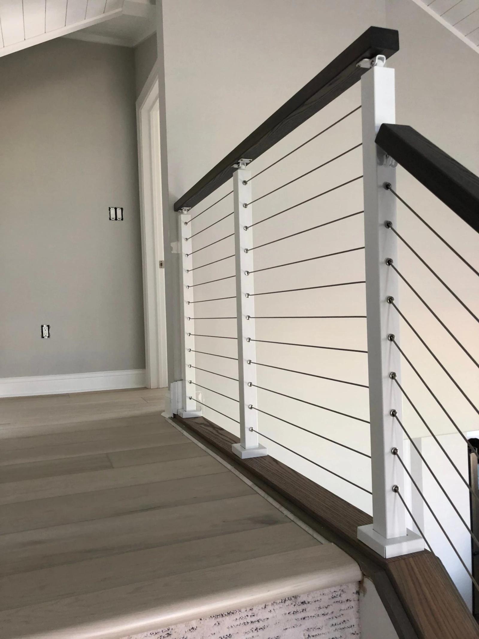 Landing railing run with white posts and dark cap beside plank flooring