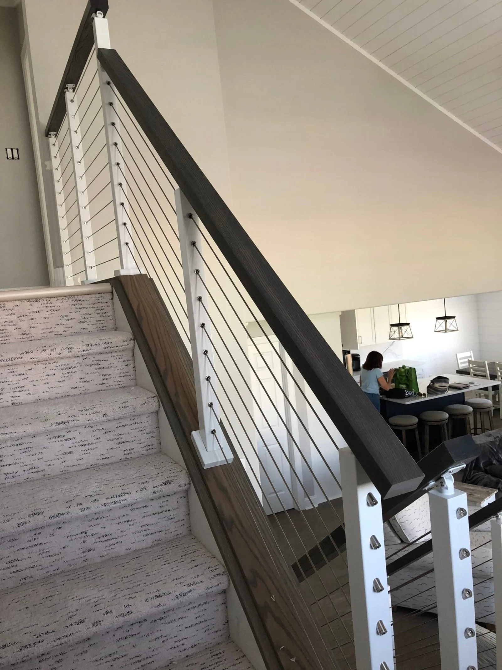 Cable railing climbing beside carpeted treads toward a dining area beyond