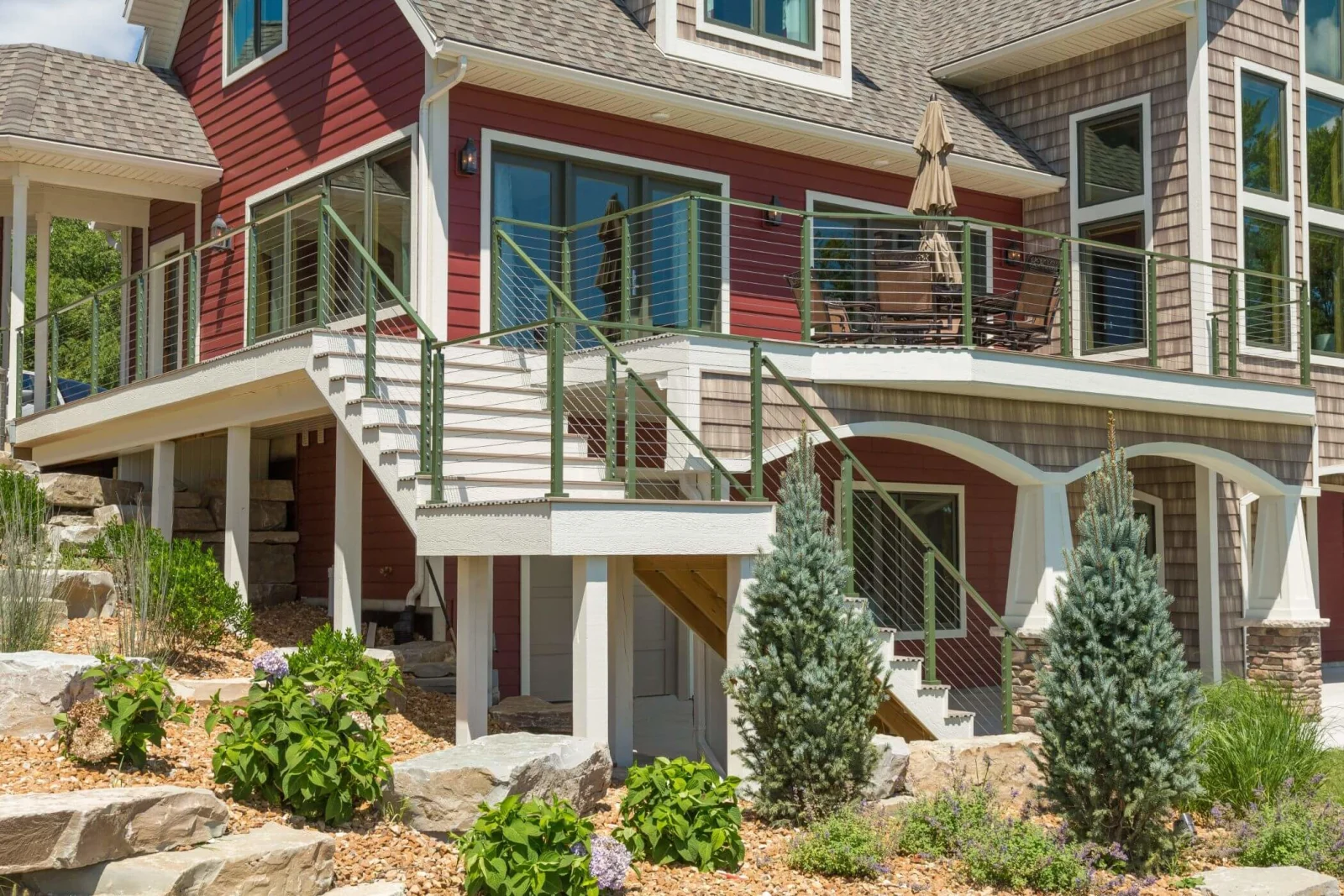 Green-painted posts and cable infill on the stairs and decks of a red lake house