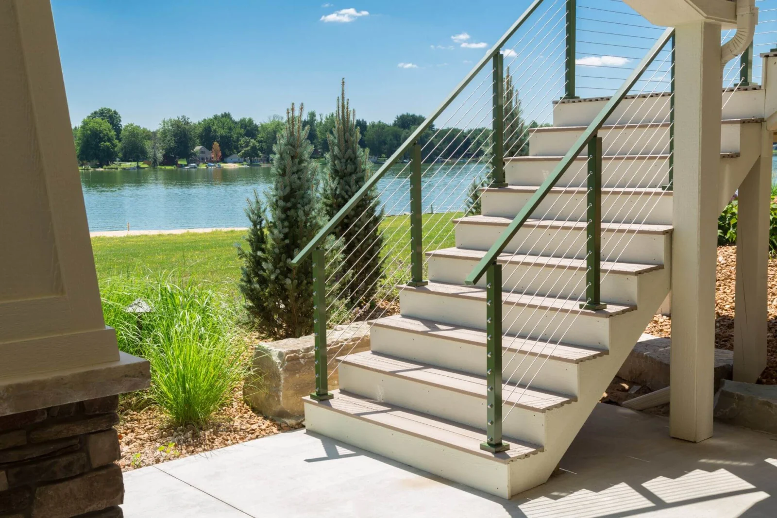 Outdoor stair with green cable railing linking a patio to the lakeside lawn