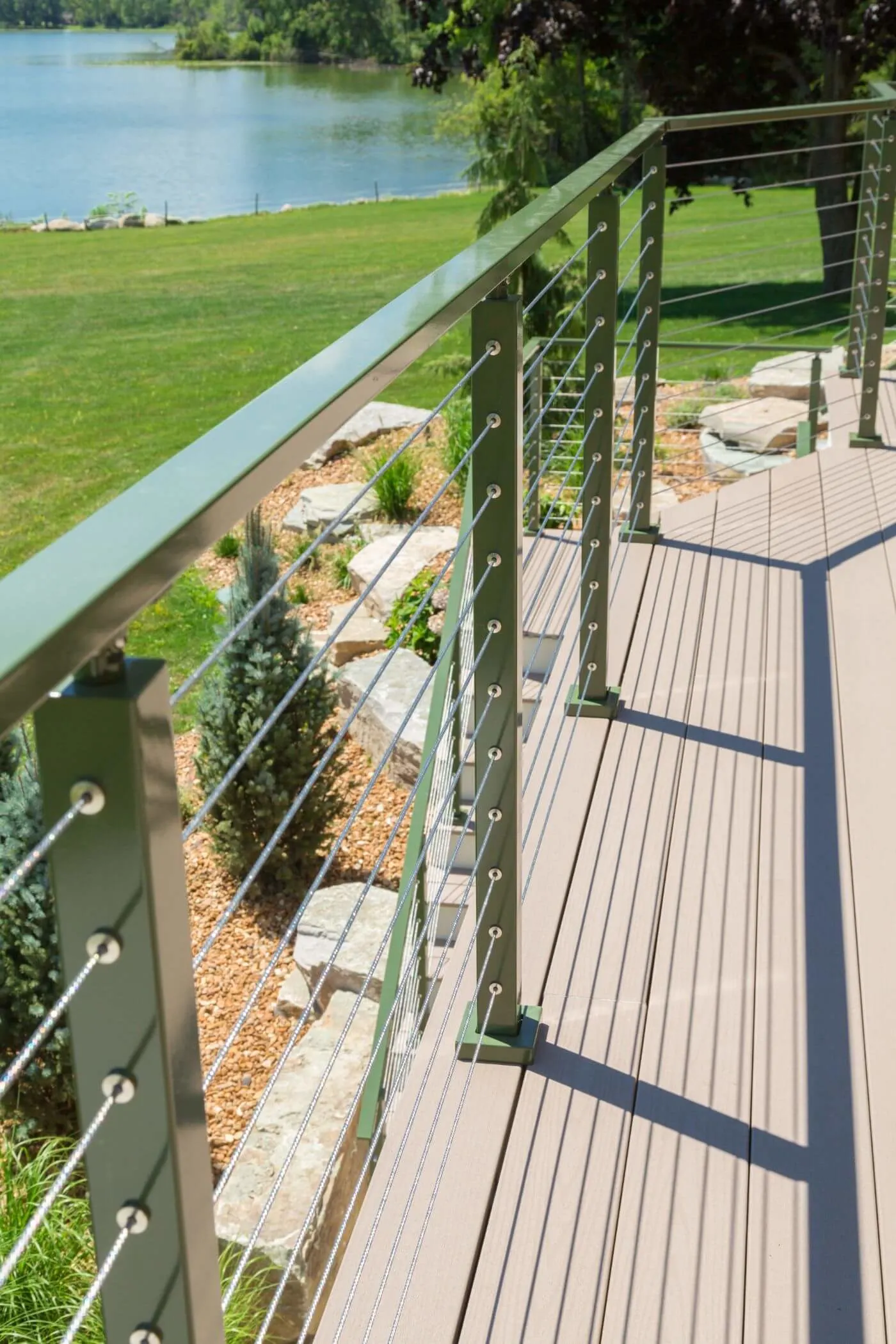 Deck walkway edged with green powder-coated cable railing above a landscaped stone bed