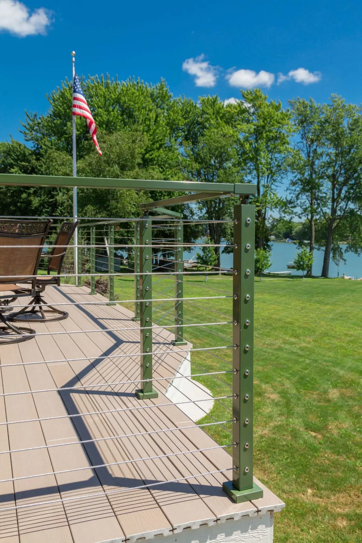 Deck corner with cable railing, a flagpole, and lake water beyond the lawn
