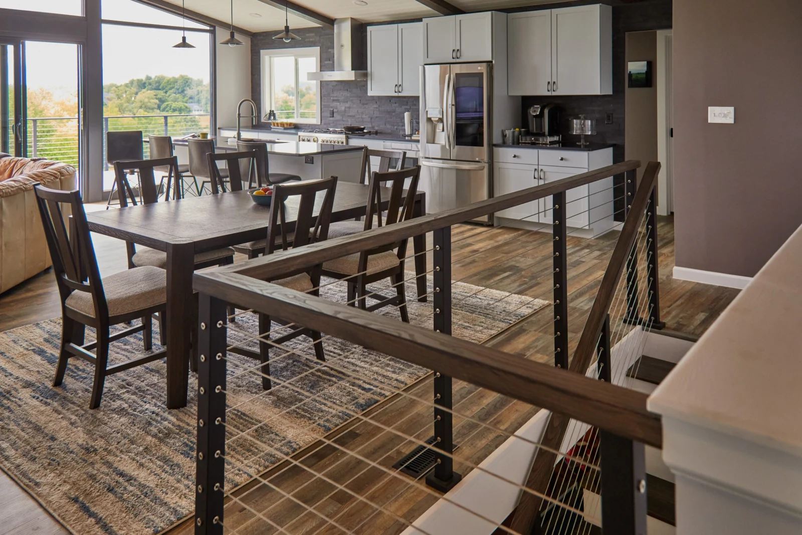 Kitchen and dining room seen past an interior cable railing with wood cap