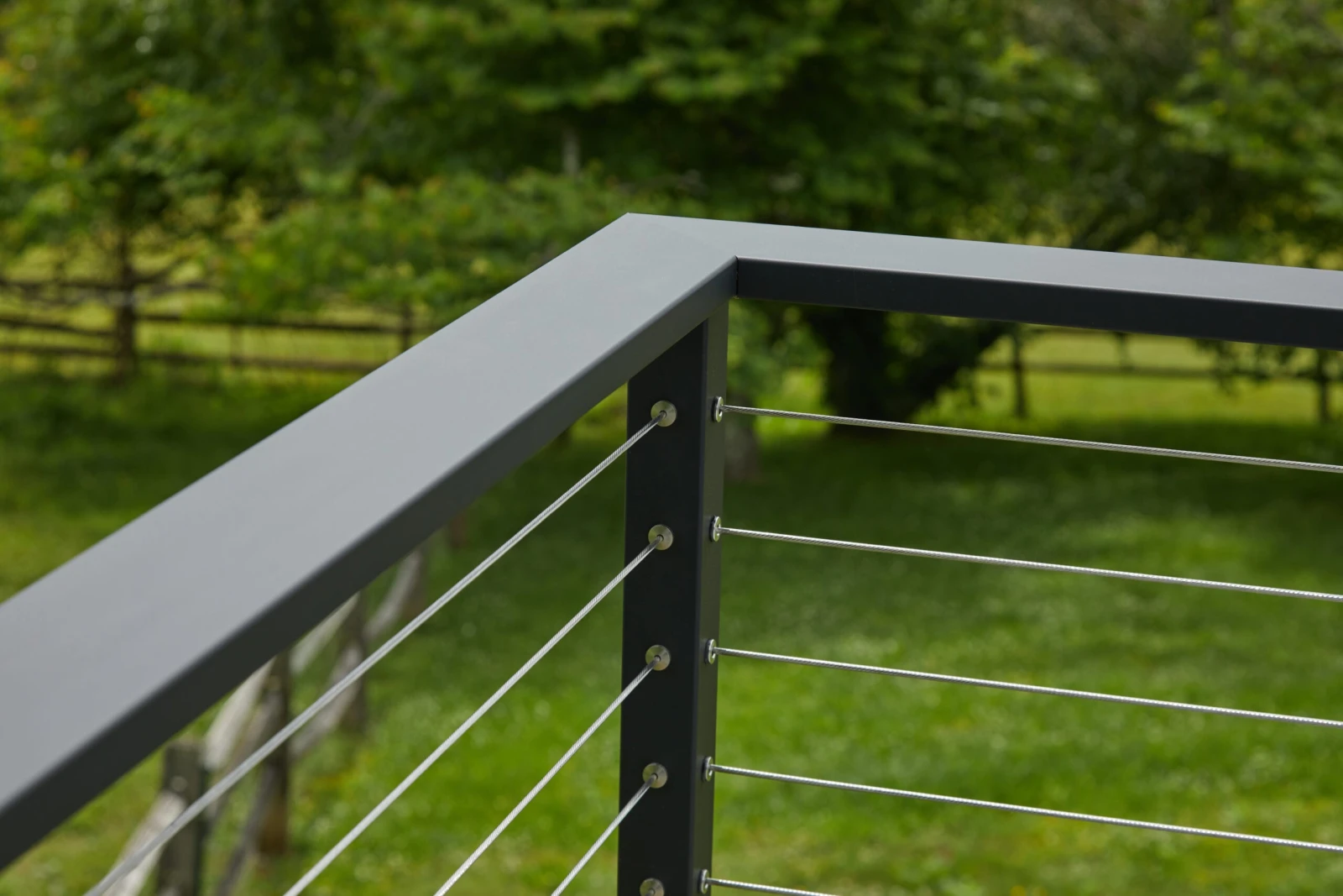 Corner detail of a black top rail with stainless cables over green lawn