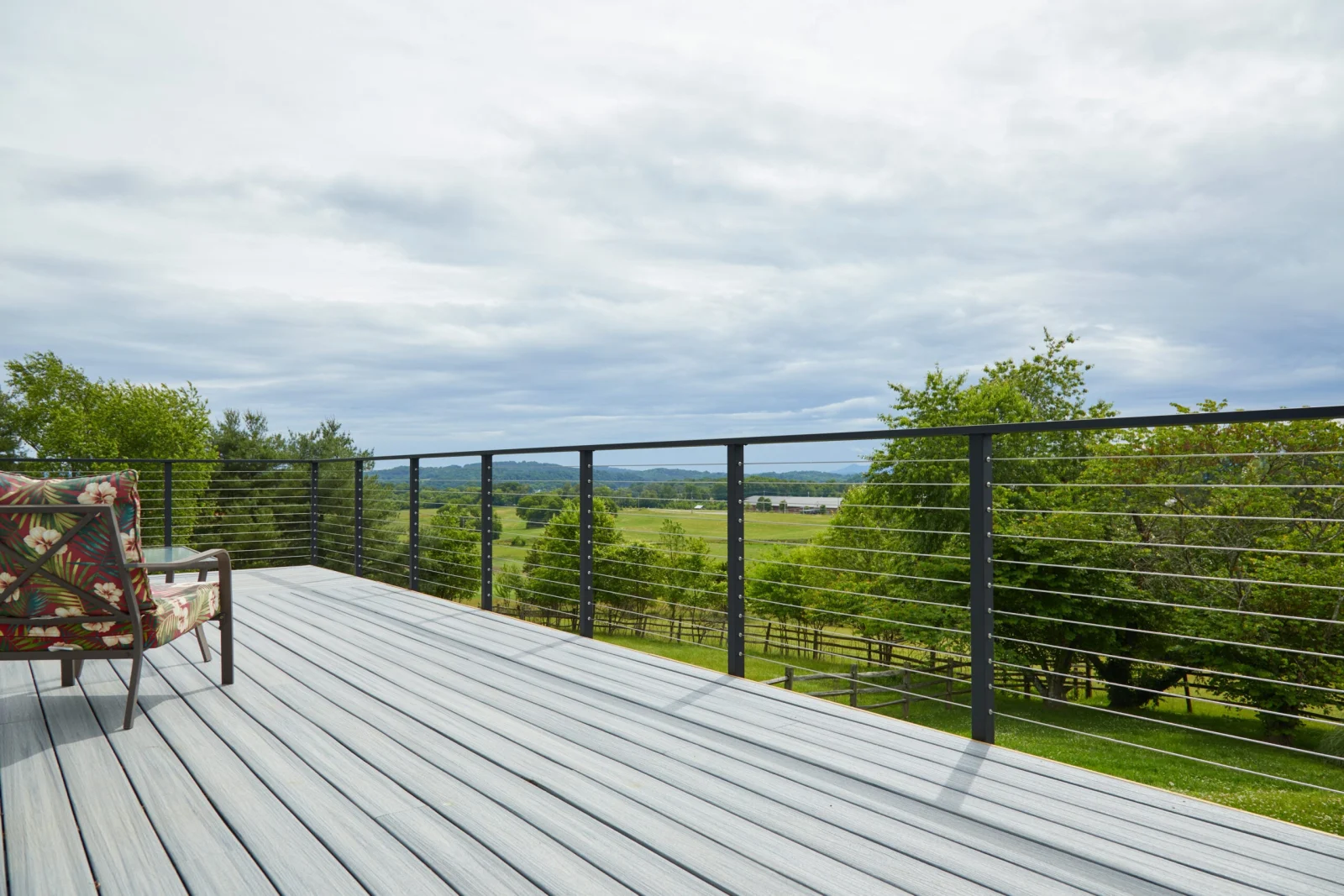 Gray deck boards and black cable railing opening to rolling farmland